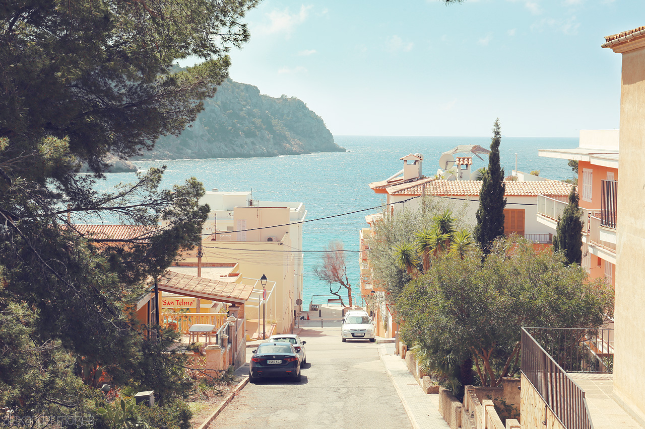 Foto von A serene glimpse down a tree-lined street in San Telmo, Mallorca, leading to the azure Mediterranean Sea.