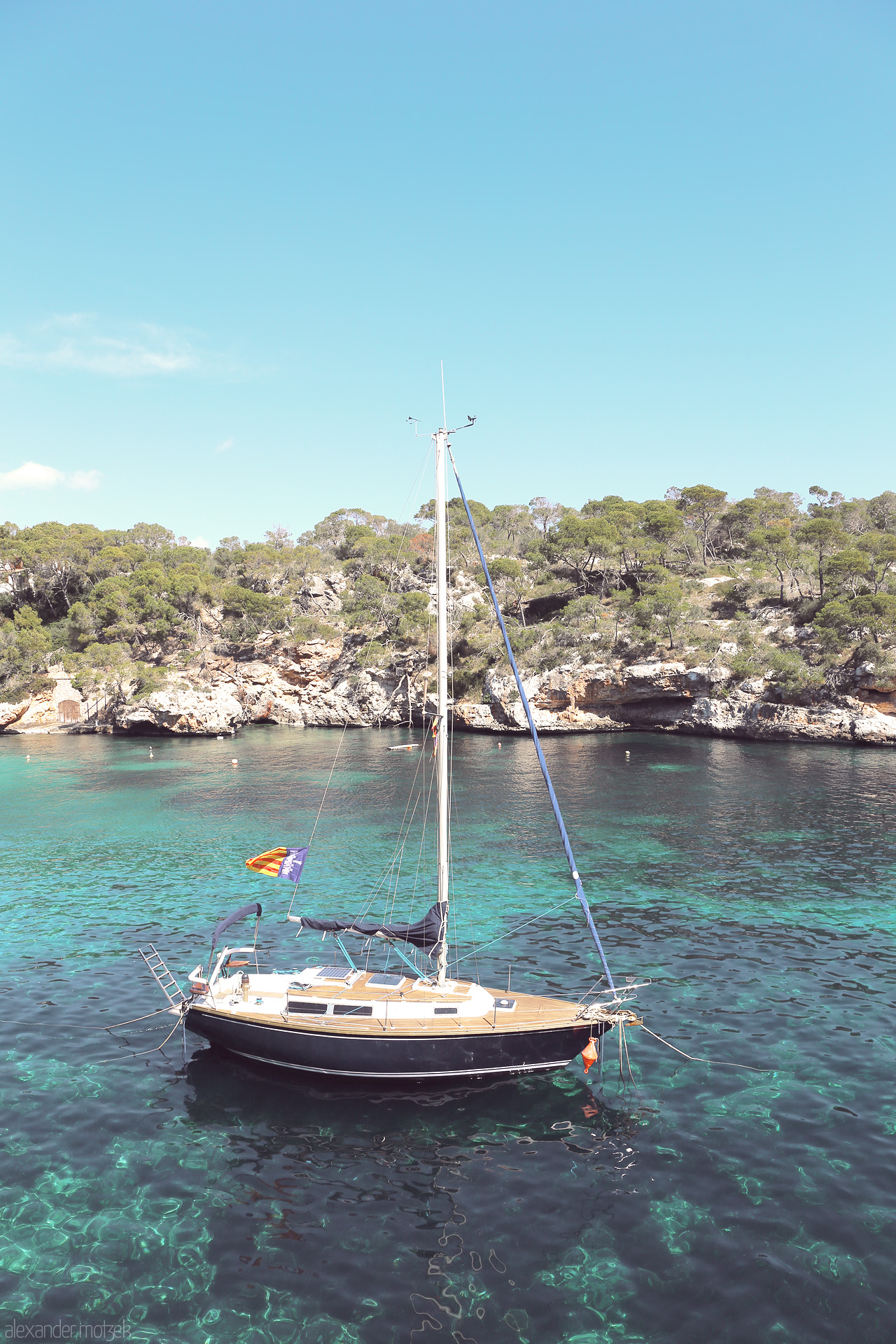 Foto von A solitary sailboat rests in the tranquil azure waters of Cala Figuera, bathed in the Mallorcan sun.