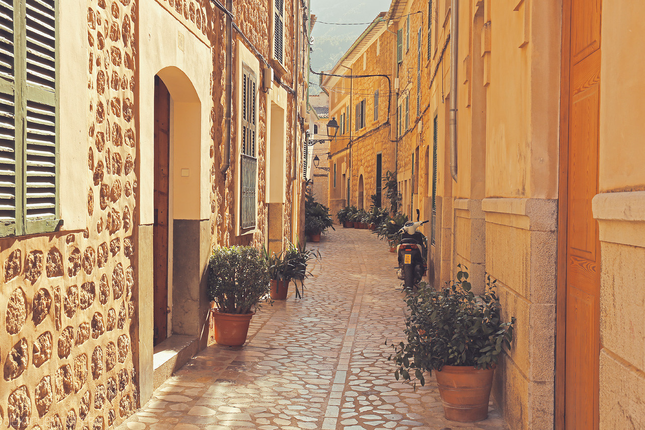 Foto von Sunlit stones grace a narrow Sóller alley, lined with traditional homes and potted plants in Mallorca.