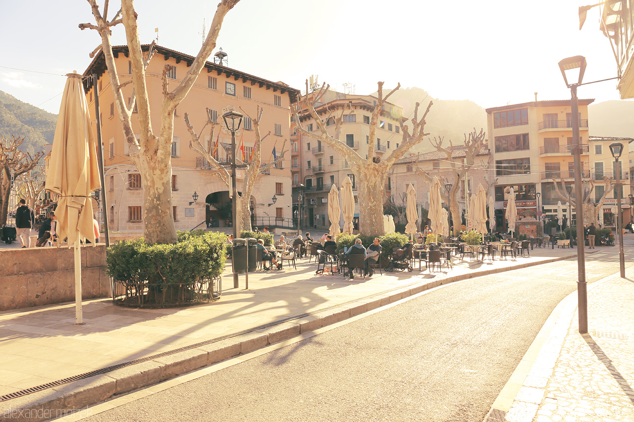Foto von Warm sunlight bathes the tranquil street cafés of Sóller, a serene scene in Mallorca's golden valley.