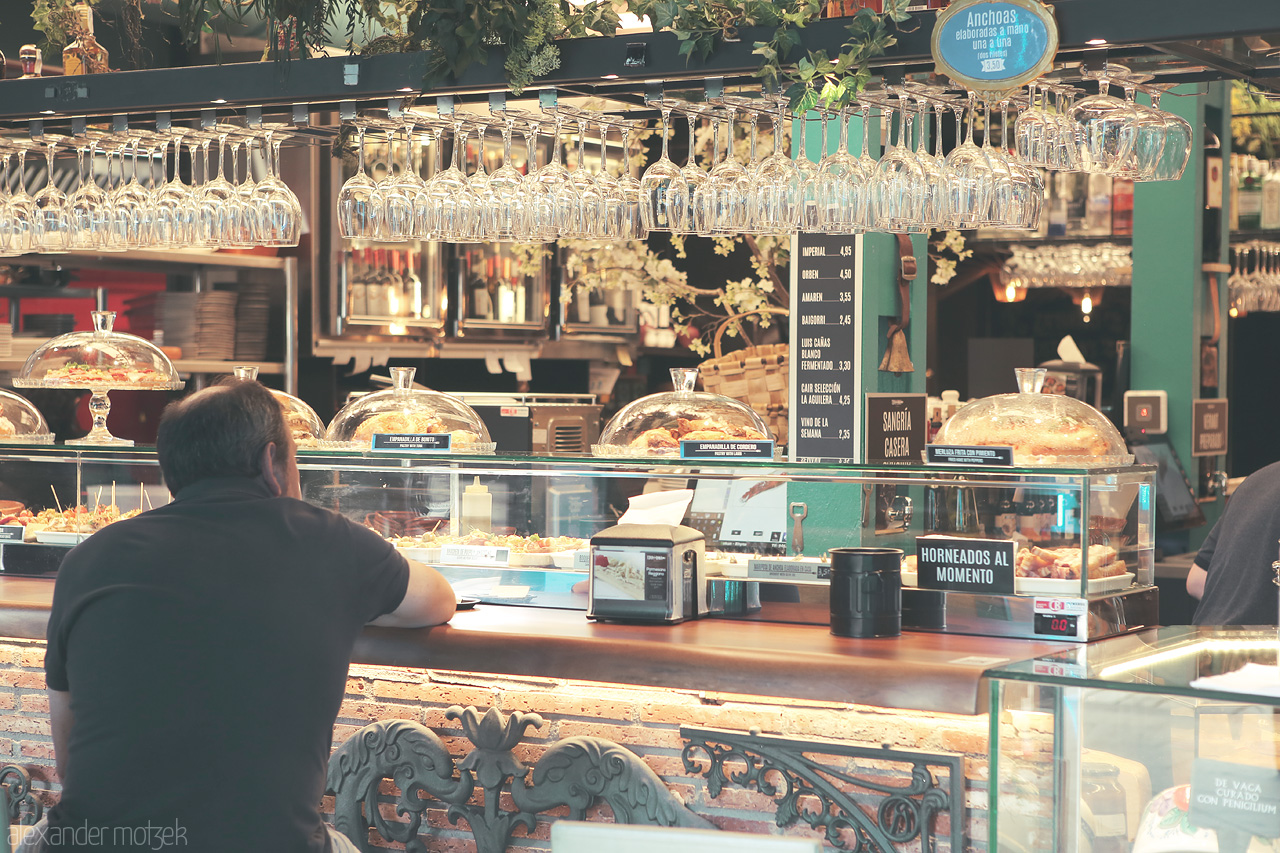Foto von A local gazes at a bar's tapas selection under glinting rows of glassware in Bilbao, Spain.