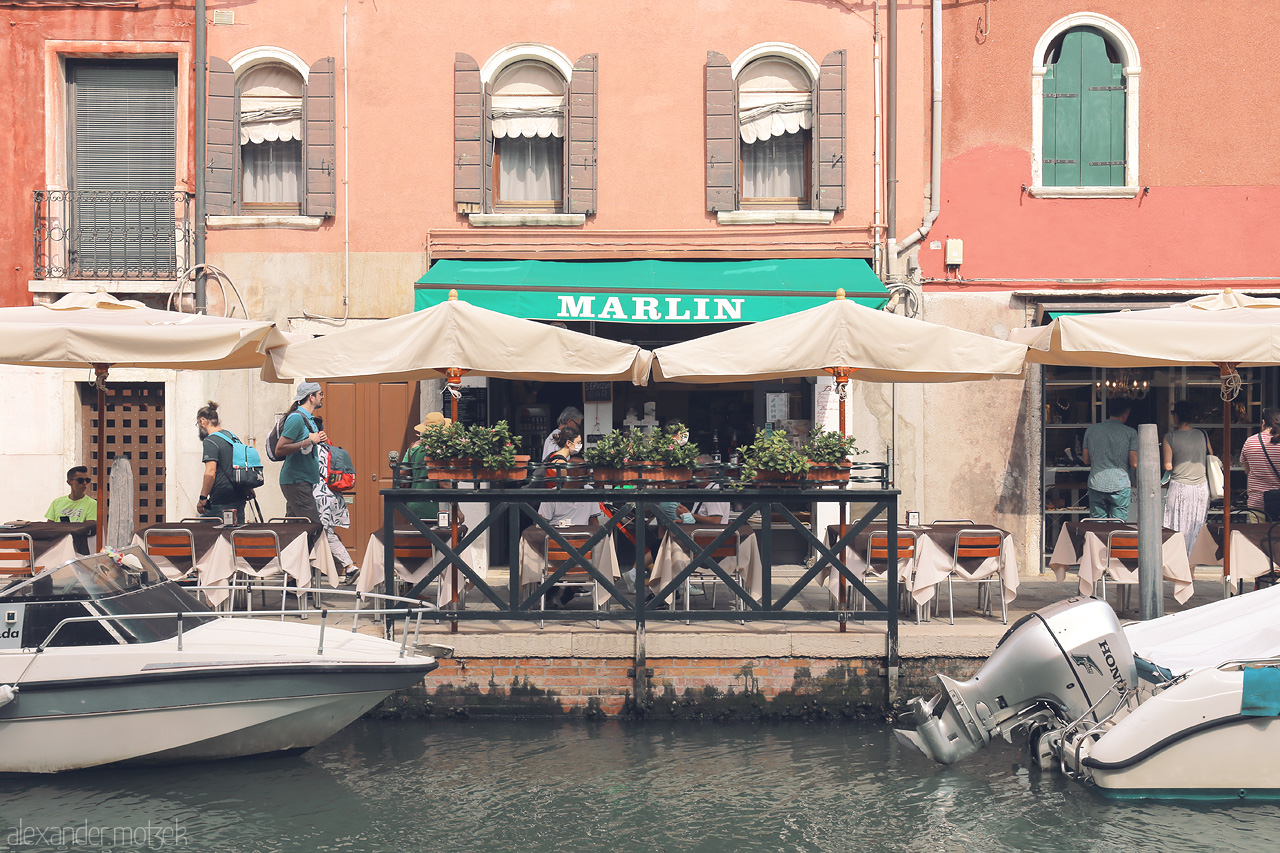 Foto von A quaint waterside café in Venice, with moored boats and bustling patrons adding to the serene Venetian charm.