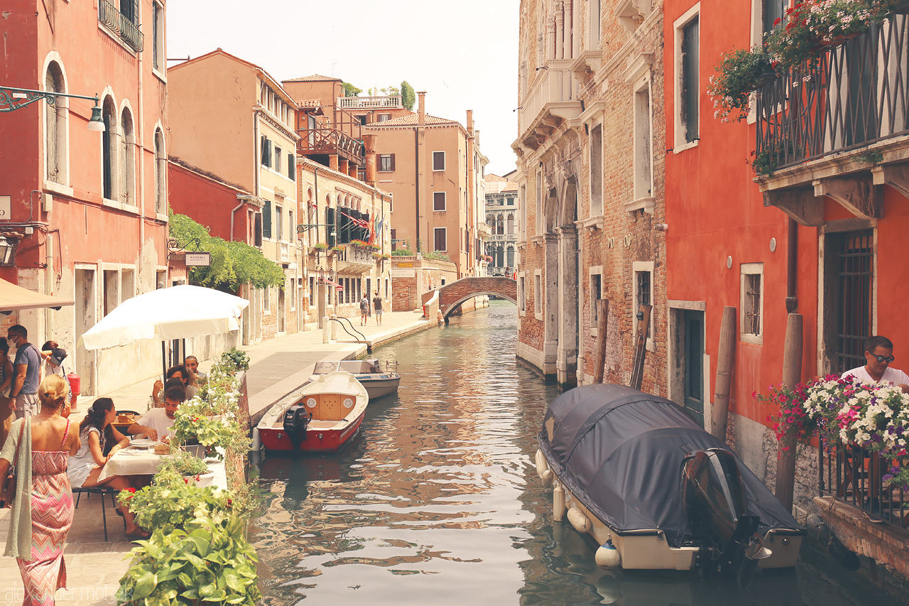 Foto von A quiet canal in Venice, with moored boats, terracotta buildings, a quaint bridge, and visitors savoring the city's charm.