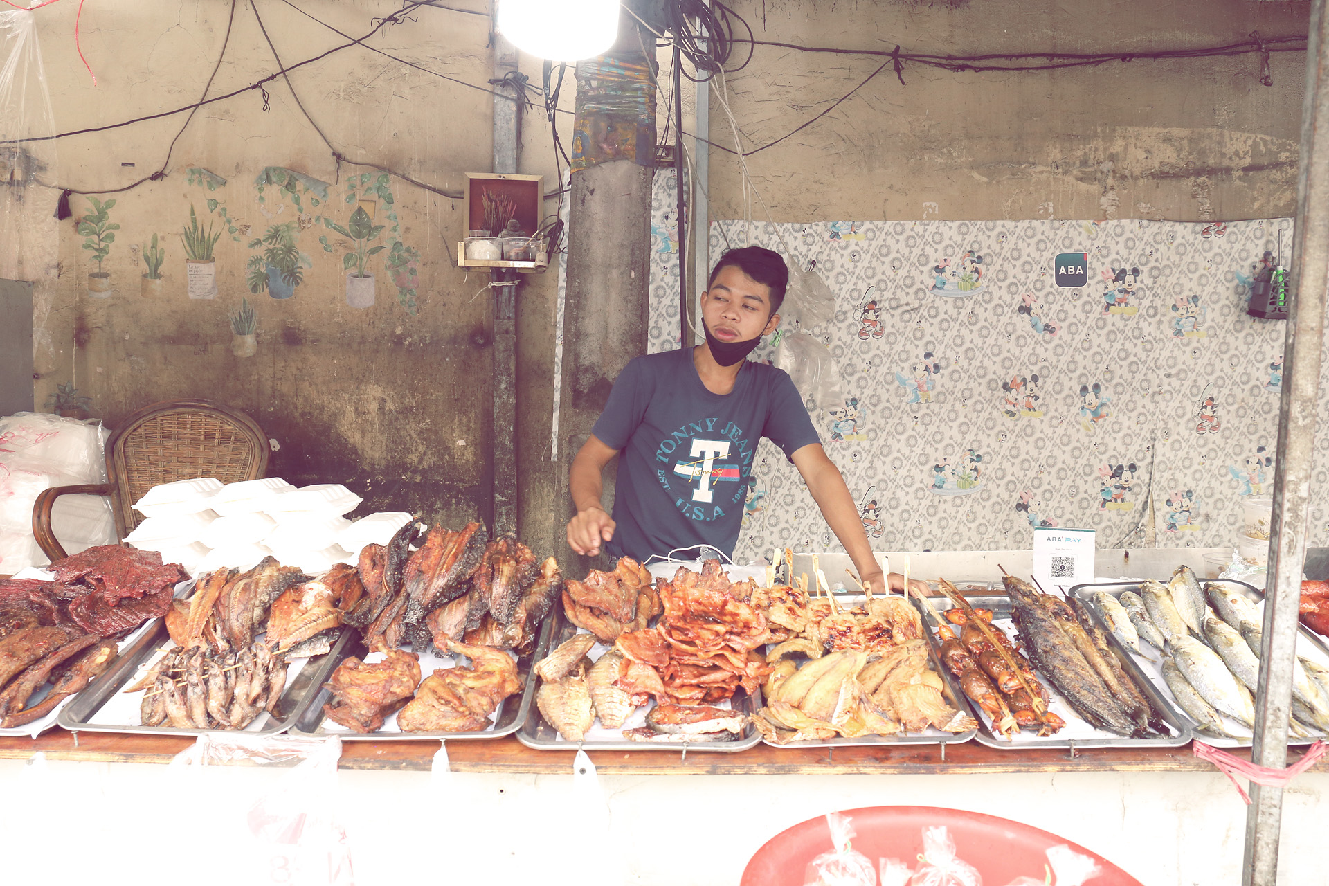 Foto von A Phnom Penh street vendor offers grilled fish and meats—local flavors lining a weathered wall in Cambodia's bustling heart.