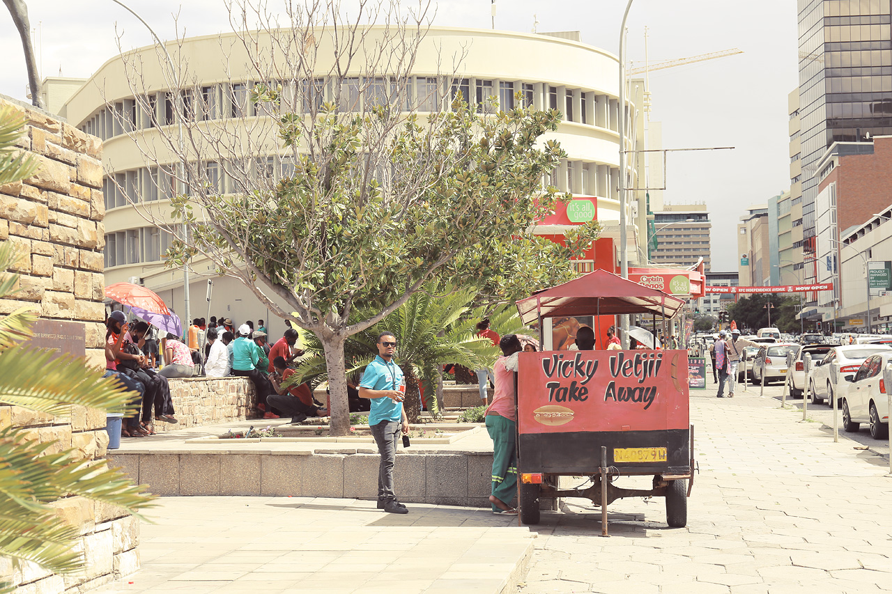 Kosmos Amongst Concret Foto von A bustling Windhoek scene with locals by a street food cart, capturing the city's vibrant everyday life.