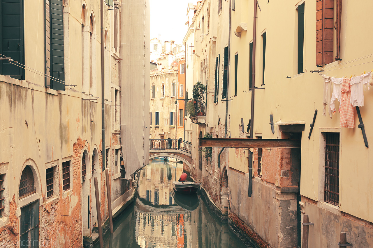 Venetian Venee Foto von A calm canal with a gondola, flanked by orange-hued buildings under the soft Venetian sun.