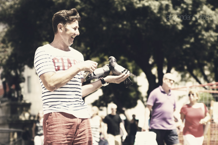 Sonrisas y Palomas Foto von A joyful moment captures a man feeding pigeons in sunny Barcelona, surrounded by vibrant life on La Rambla.