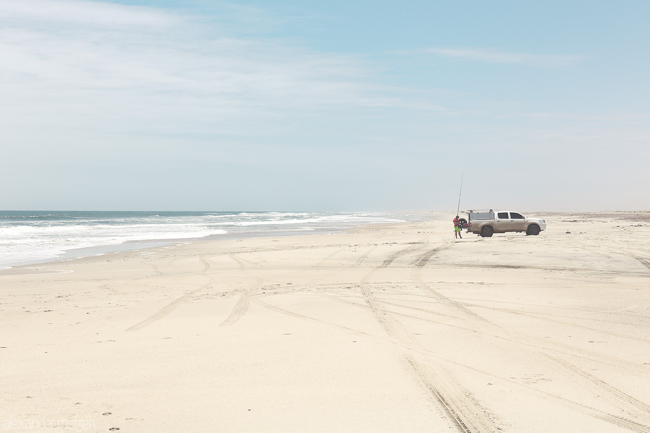 Namib's Coastal Mirage Foto von A lone vehicle and figures against the vastness of Skeleton Coast, Namibia, where desert meets ocean.