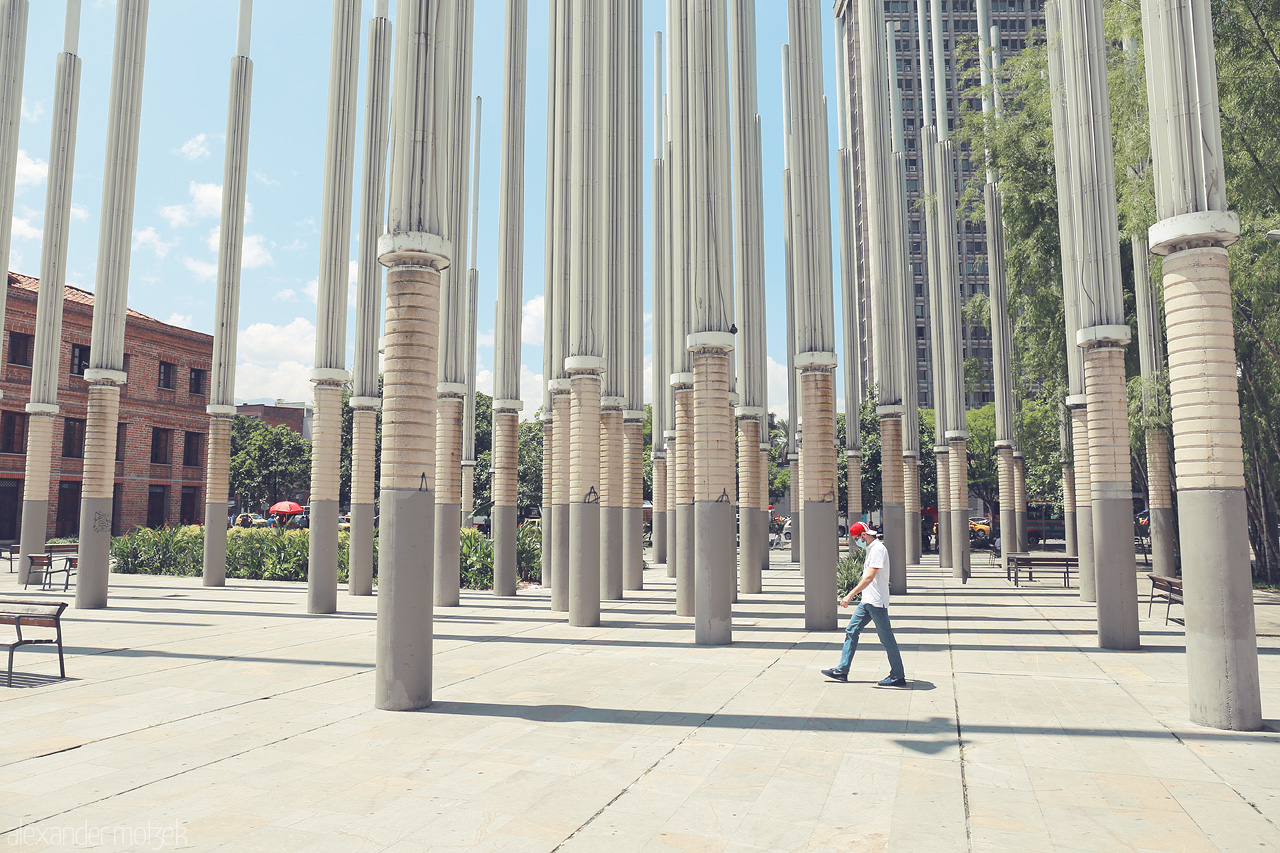 Columnas de Luz Foto von A man walks through tall columns in Comuna 10 - La Candelaria, Medellín, Colombia, offering a glimpse of the vibrant urban life.