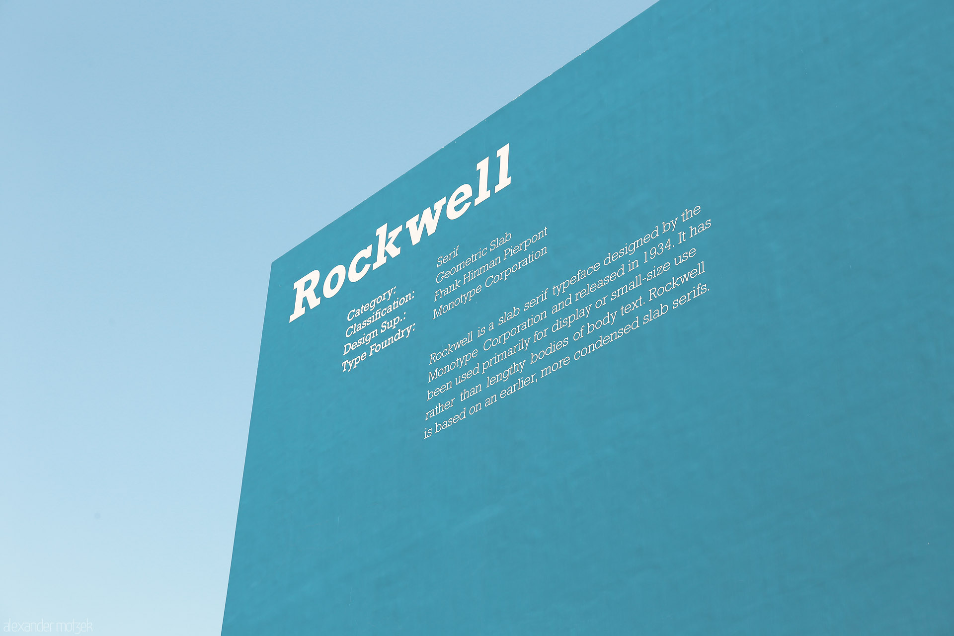 Hajar & Sky Foto von A minimalist blue wall in Dubai, adorned with 'Rockwell' typography, rises sharply under the clear Emirati sky.