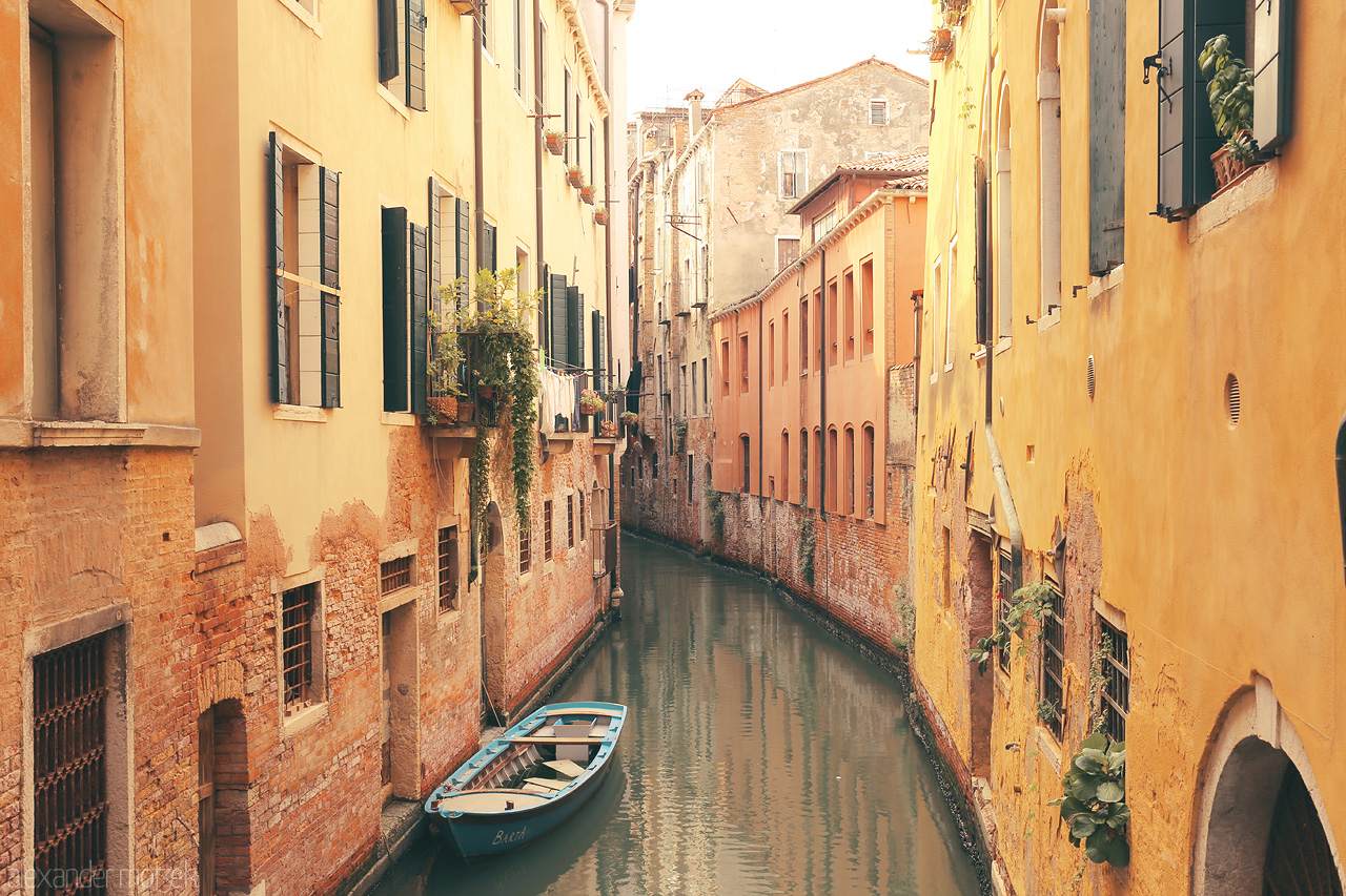 Acqua Segreta Foto von A serene canal in Venice, lined by sun-kissed buildings with a lone boat, encapsulating the city's timeless charm.