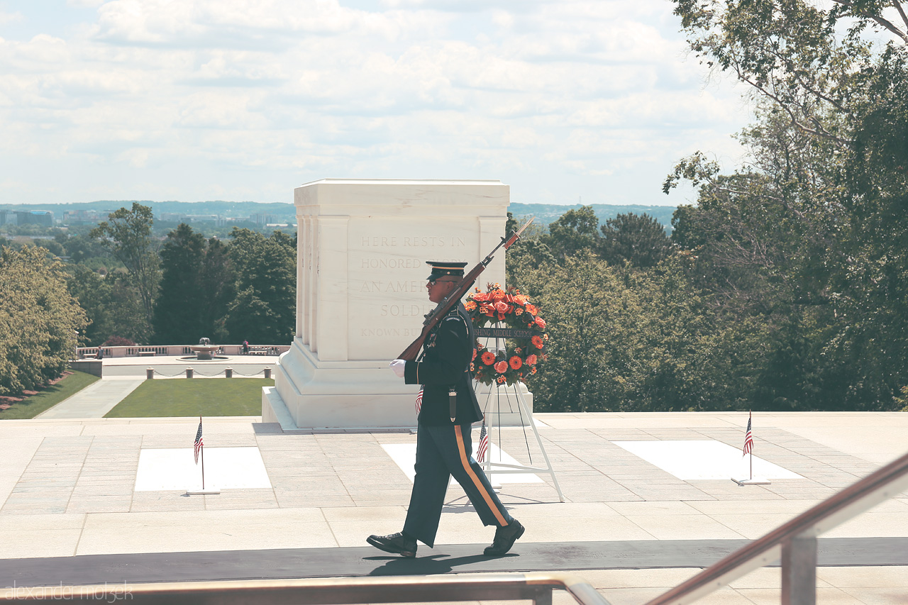 Vigil at Arlington Foto von A solemn soldier marches at the Tomb of the Unknowns in Arlington, Virginia, under the gentle embrace of nature's watchful gaze.