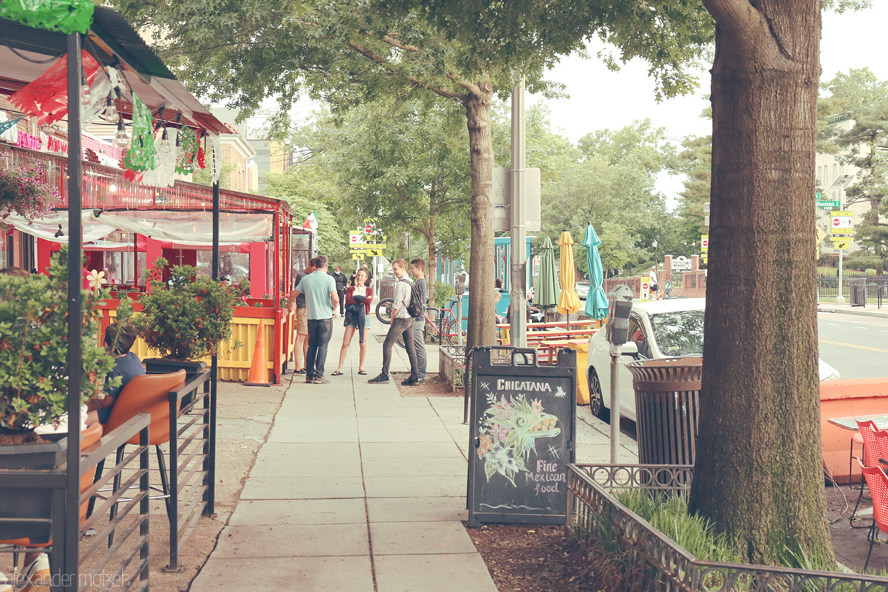 Capitol Stroll Serenity Foto von A vibrant sidewalk in Washington, D.C. showcases al fresco dining, lively foliage, and a hint of urban charm, capturing the city's bustling spirit.