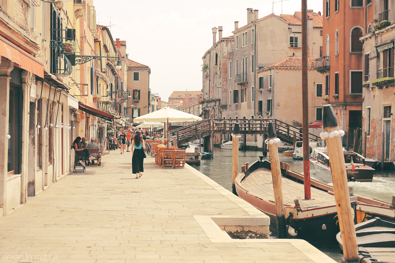 Venetian Vistas Foto von A warm day in Venice, with gondolas docked along a serene canal flanked by historic buildings and lively terraces.