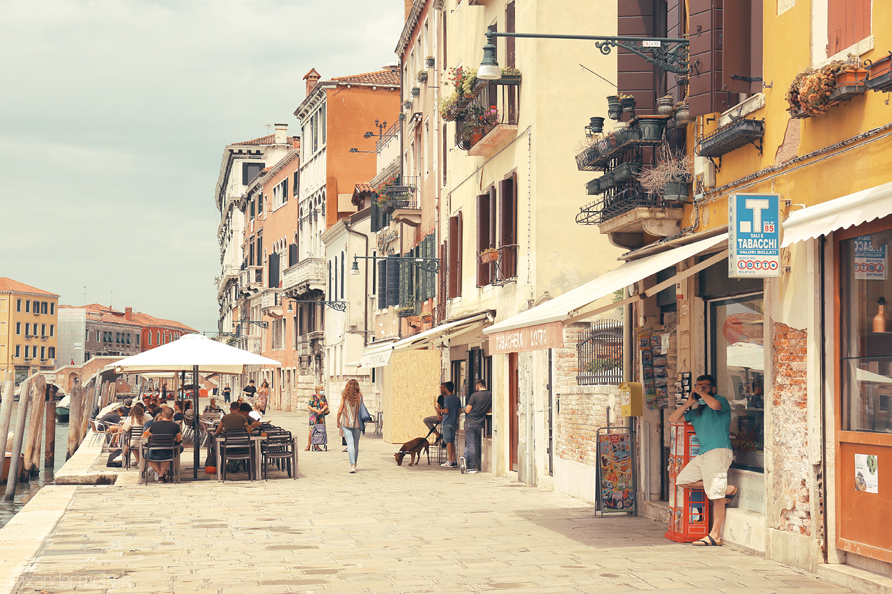 Calle Cromatica Foto von Cafes and boutiques line a Venetian street, echoing with the murmur of a lively afternoon in Venice.
