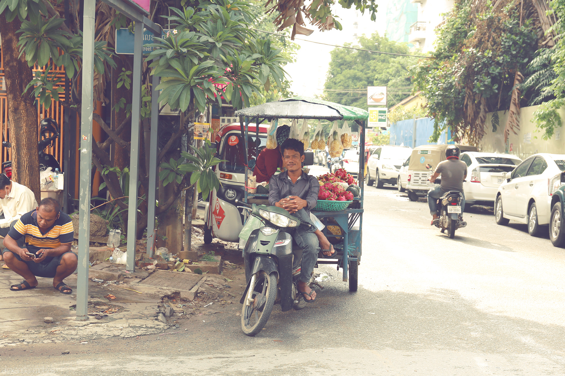 Phsar Nom Pan: Street Symphony Foto von A street vendor on his moto-cart offers bright dragonfruit and snacks on a typical sunlit Phnom Penh street, Cambodia.