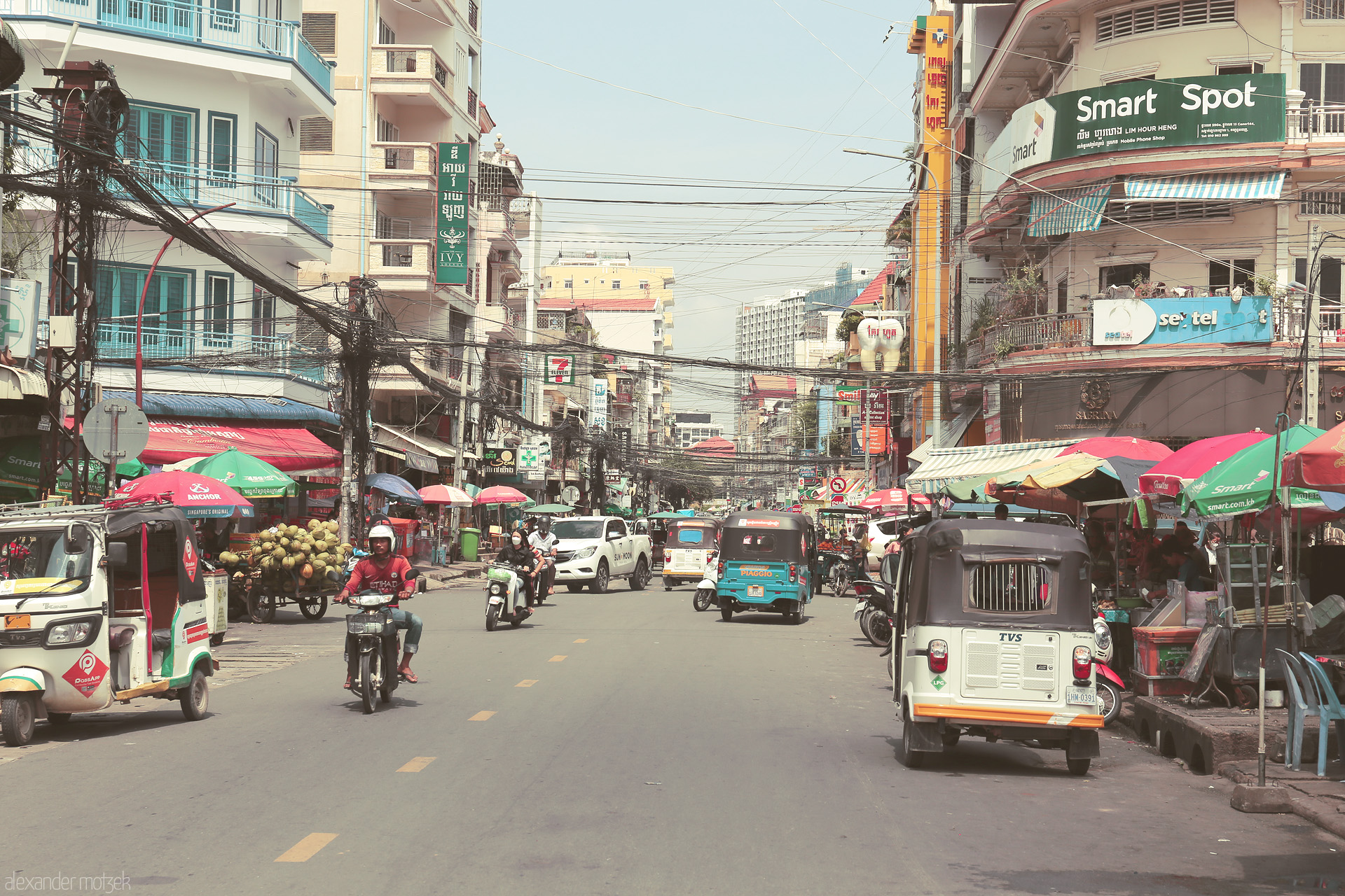 Coconut Currents Foto von Bustling tuk tuks and vibrant markets color a typical Phnom Penh street, alive under tangled wires and Khmer signs.