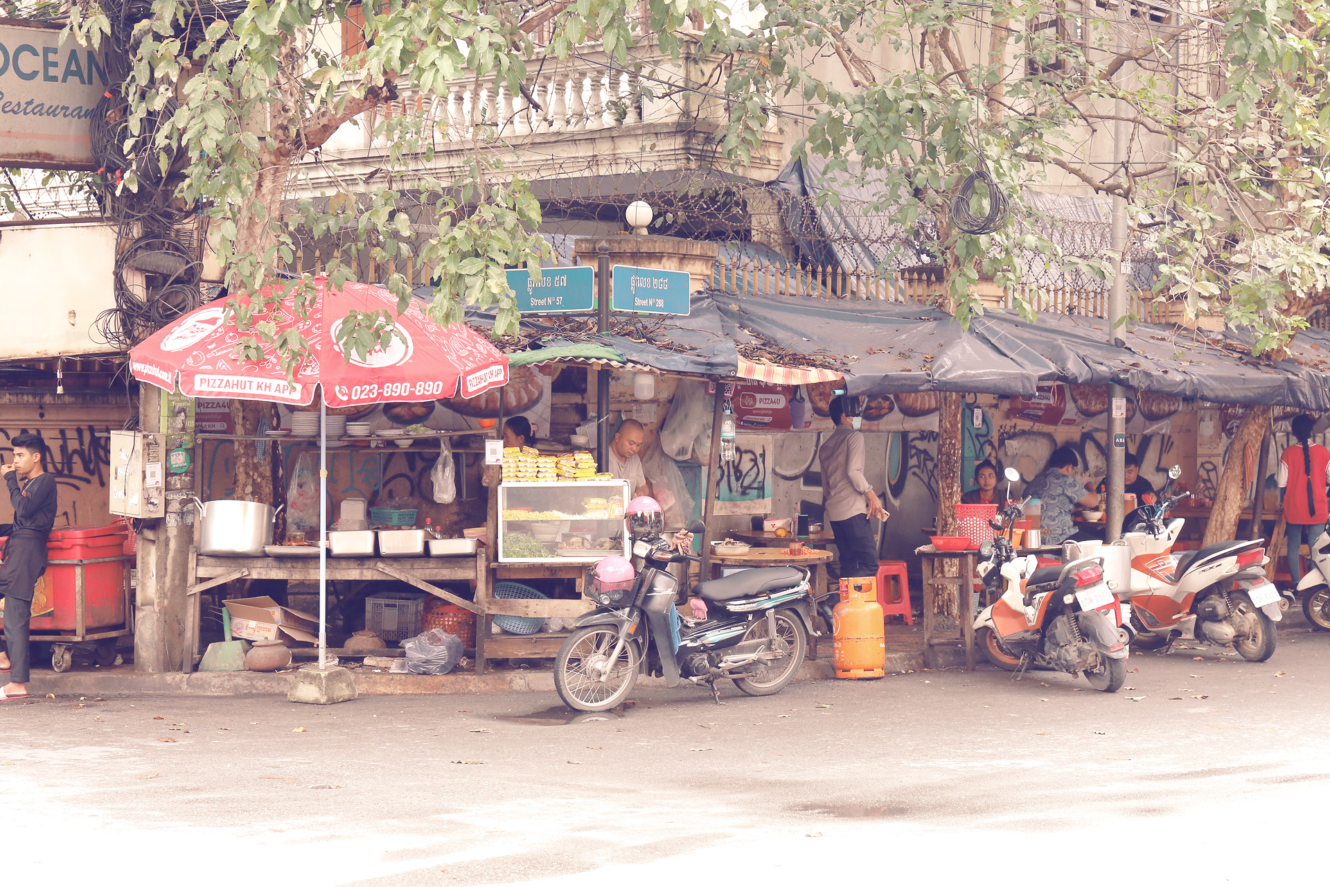 Streetside Sâbai Foto von Local street food stalls bustle under leafy shade, scooters parked in vibrant Phnom Penh, Cambodia, on bustling Street 136.
