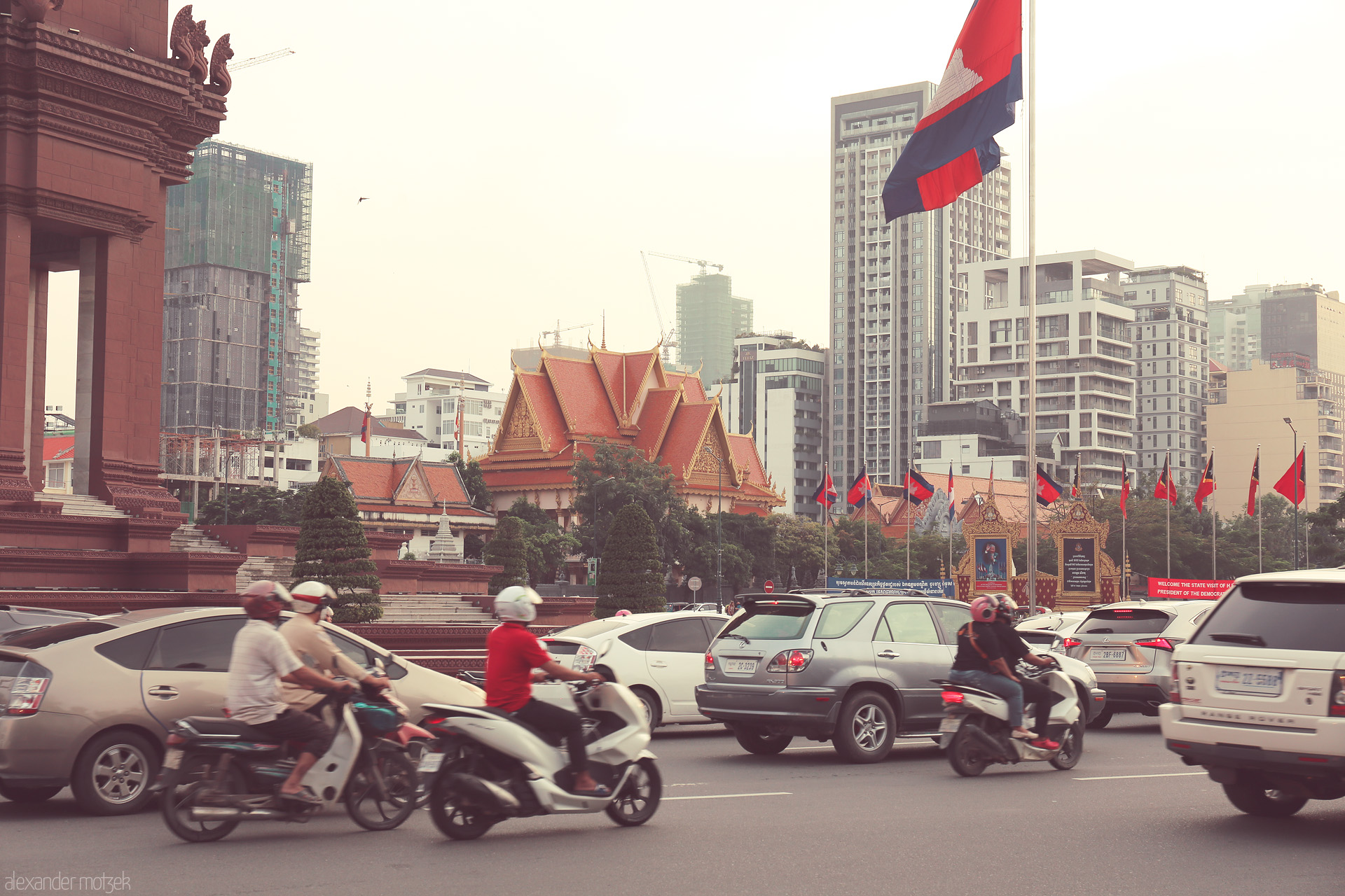 Phnom Penh Pulse Foto von Rush hour in Phnom Penh: scooters zip past monuments and golden temples, modern towers rising in Cambodia's heart.