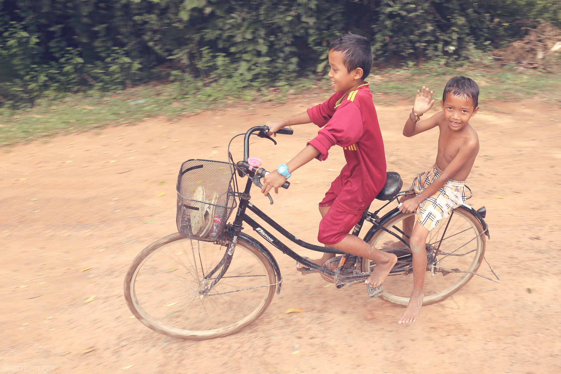 Angkor Smiles Foto von Two Khmer boys on a bicycle, grinning and carefree, ride a dusty path near Angkor Wat, Siem Reap, capturing the spirit of Cambodian youth.