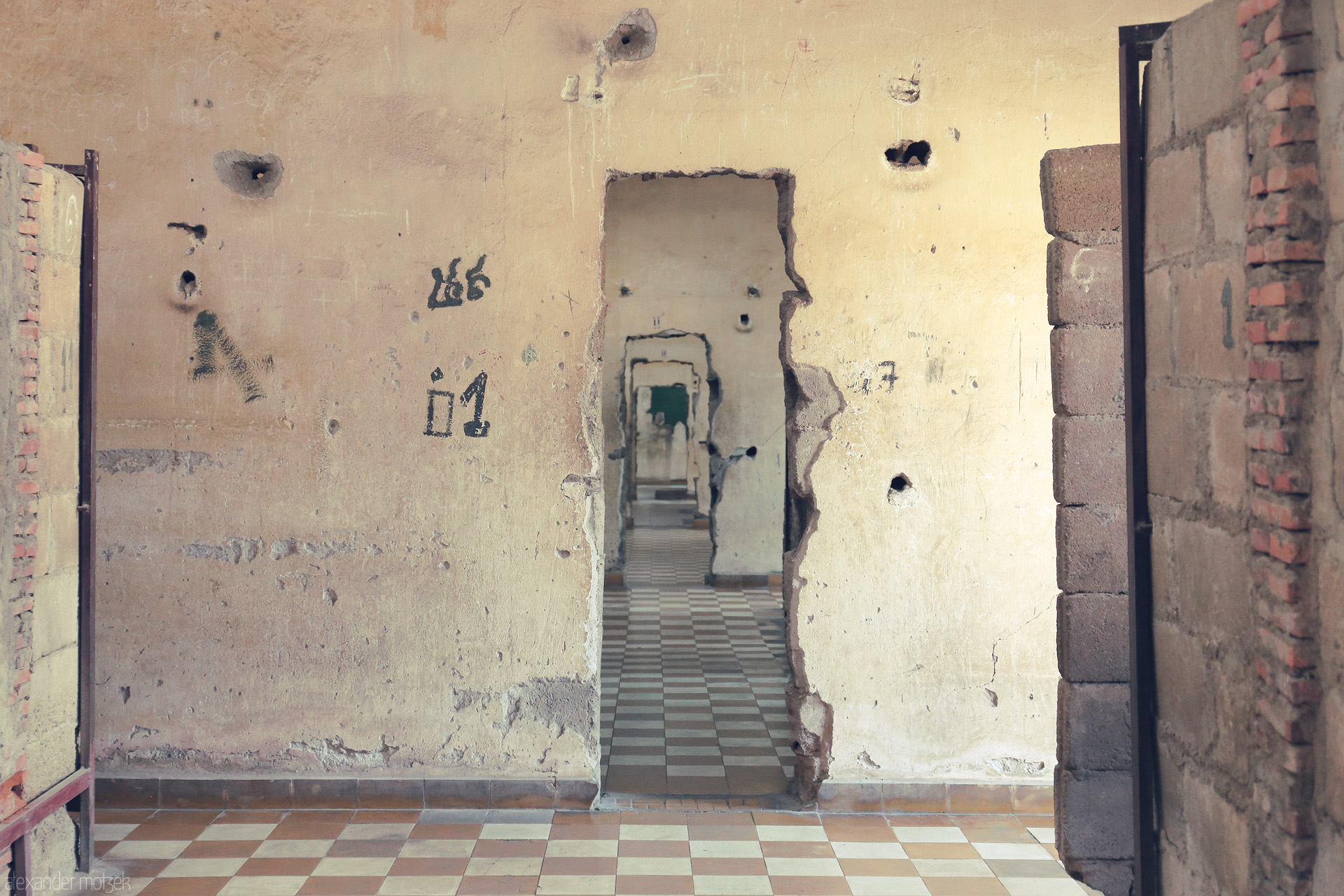 Chbab Dach | Echoes Foto von War-torn walls in Phnom Penh’s Tuol Sleng, doors and scars echo Cambodia’s haunted past, stillness woven into each fading tile and memory.