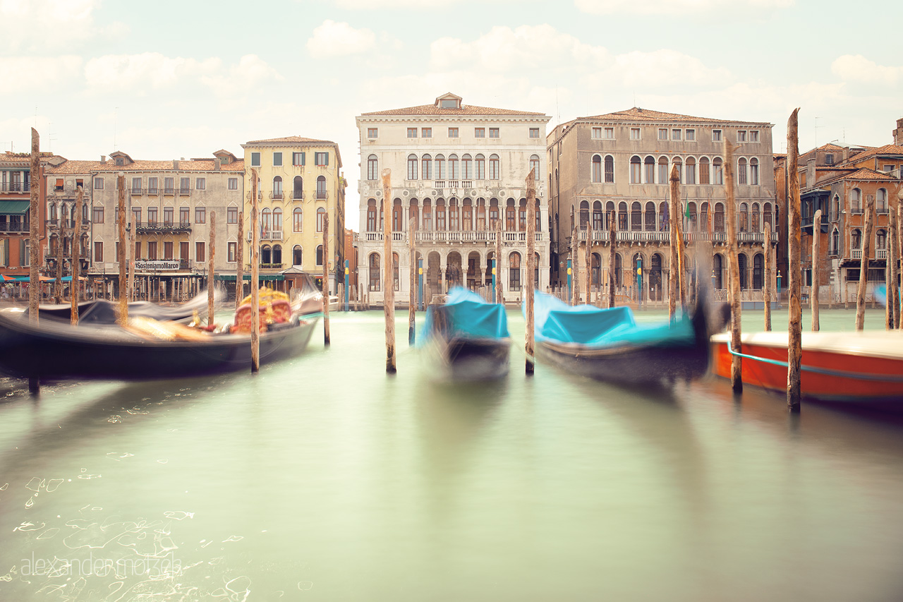 Gondole Alla Brezza Foto von Gondolas blur in motion on serene Venetian waters, timeless facades backdrop under a sunlit sky.