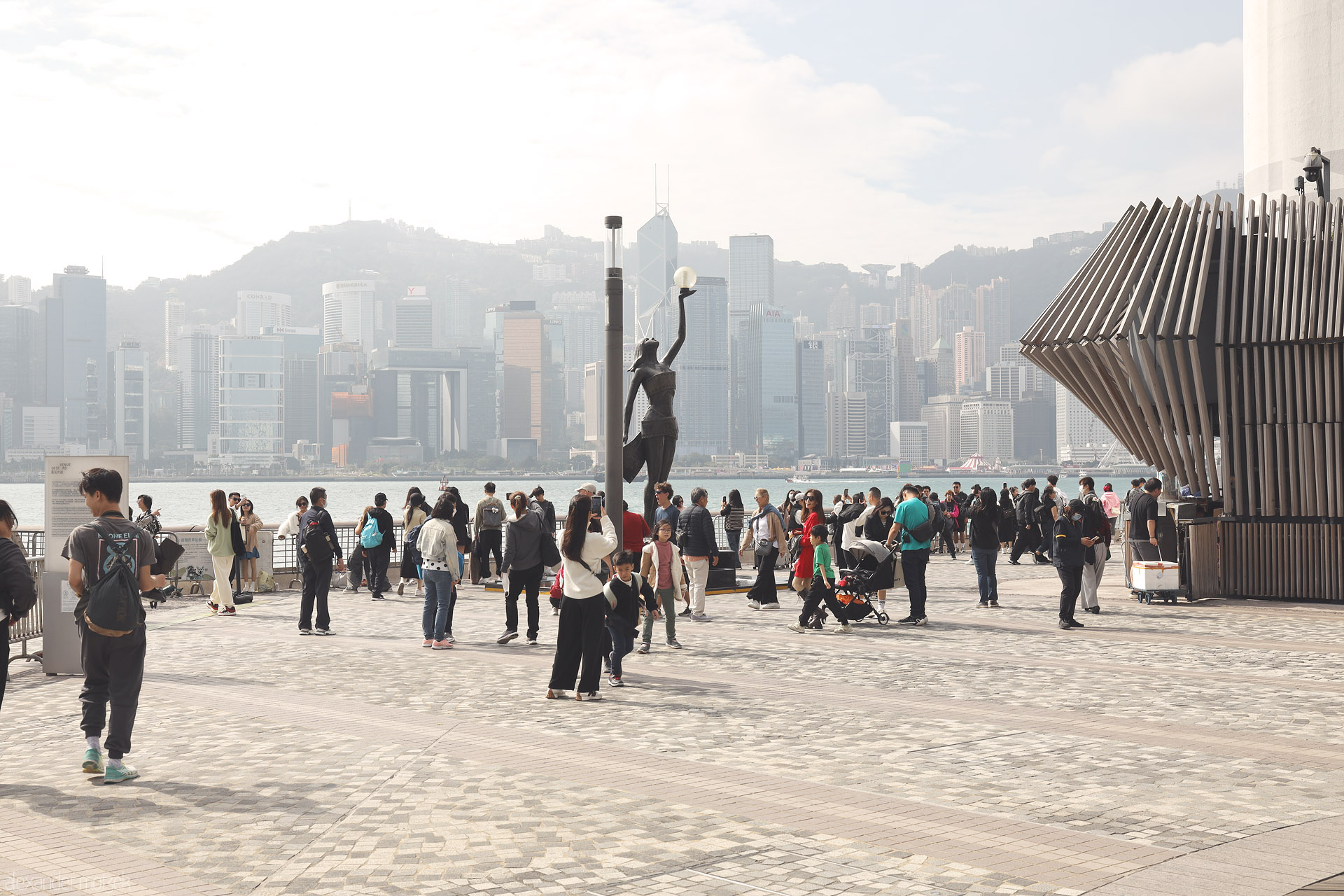 Foto von Visitors gather on the Avenue of Stars, Tsim Sha Tsui, Kowloon, looking across Victoria Harbour to Hong Kong Island’s hazy skyline.