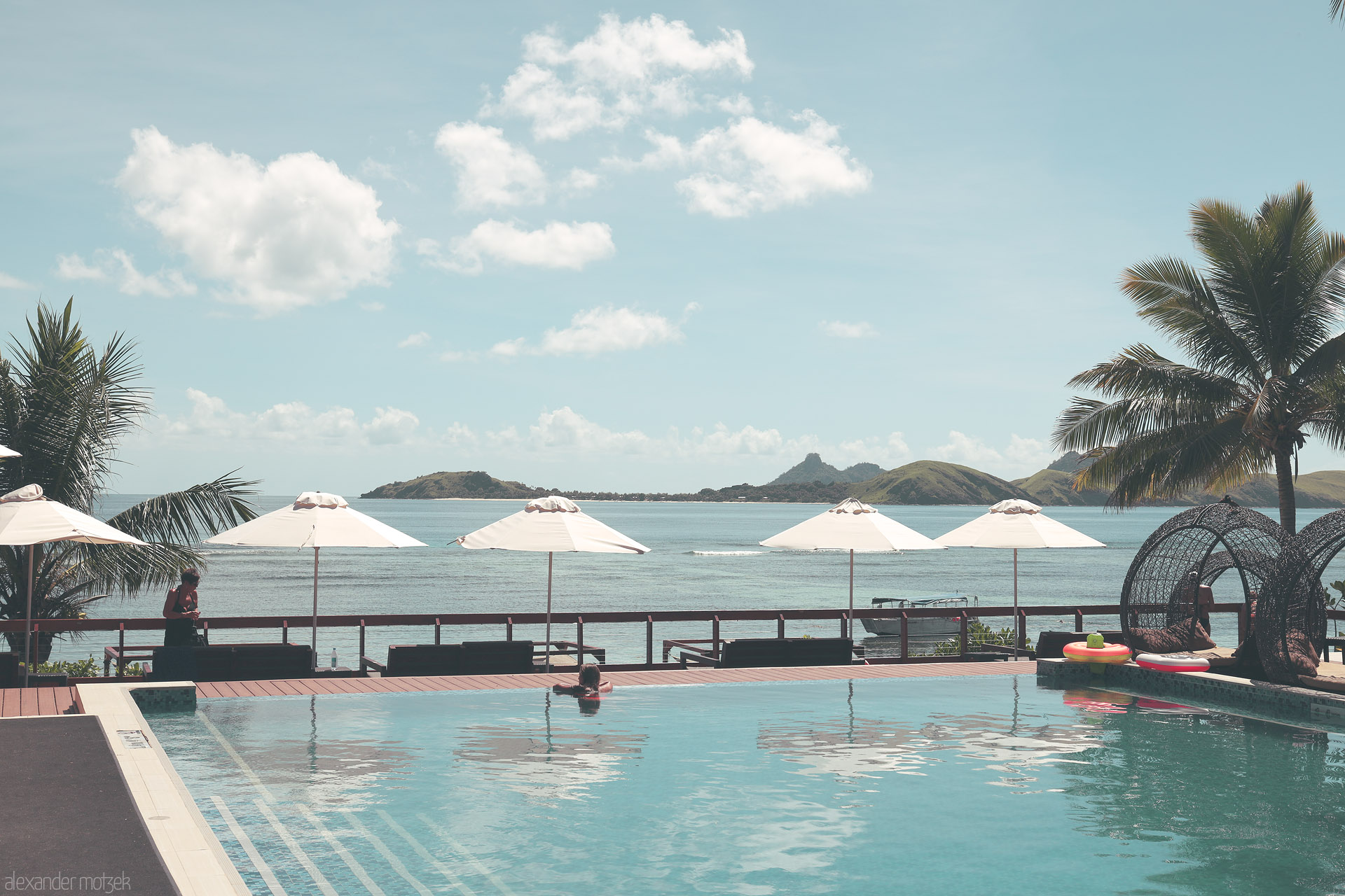 Foto von Infinity pool and white umbrellas facing a calm lagoon and green Mamanuca islets under soft clouds, Tokoriki, Fiji.