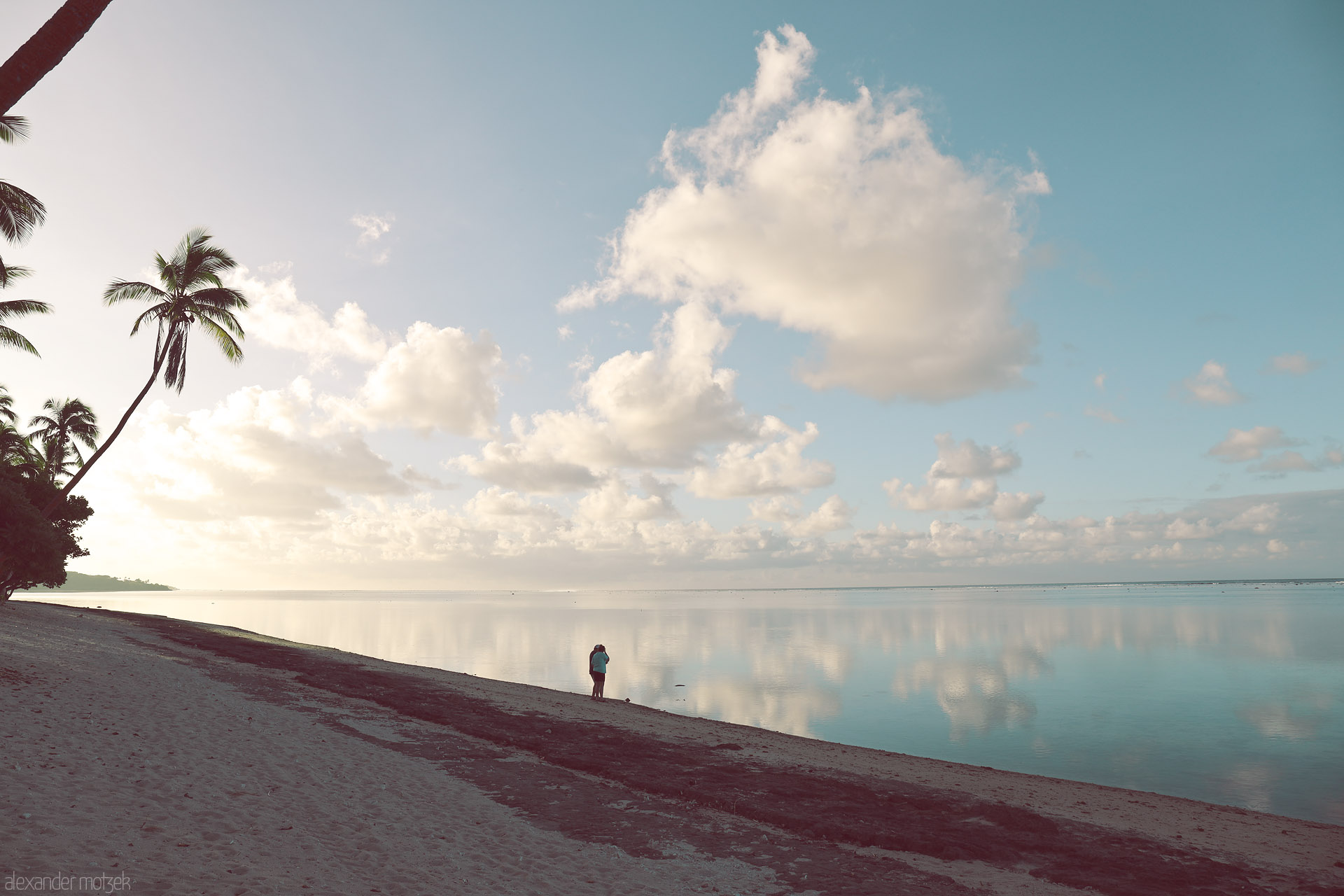 Foto von Lone figure on a palm-fringed beach at dawn, clouds mirrored on a glassy lagoon, Yanuca Island, Fiji.