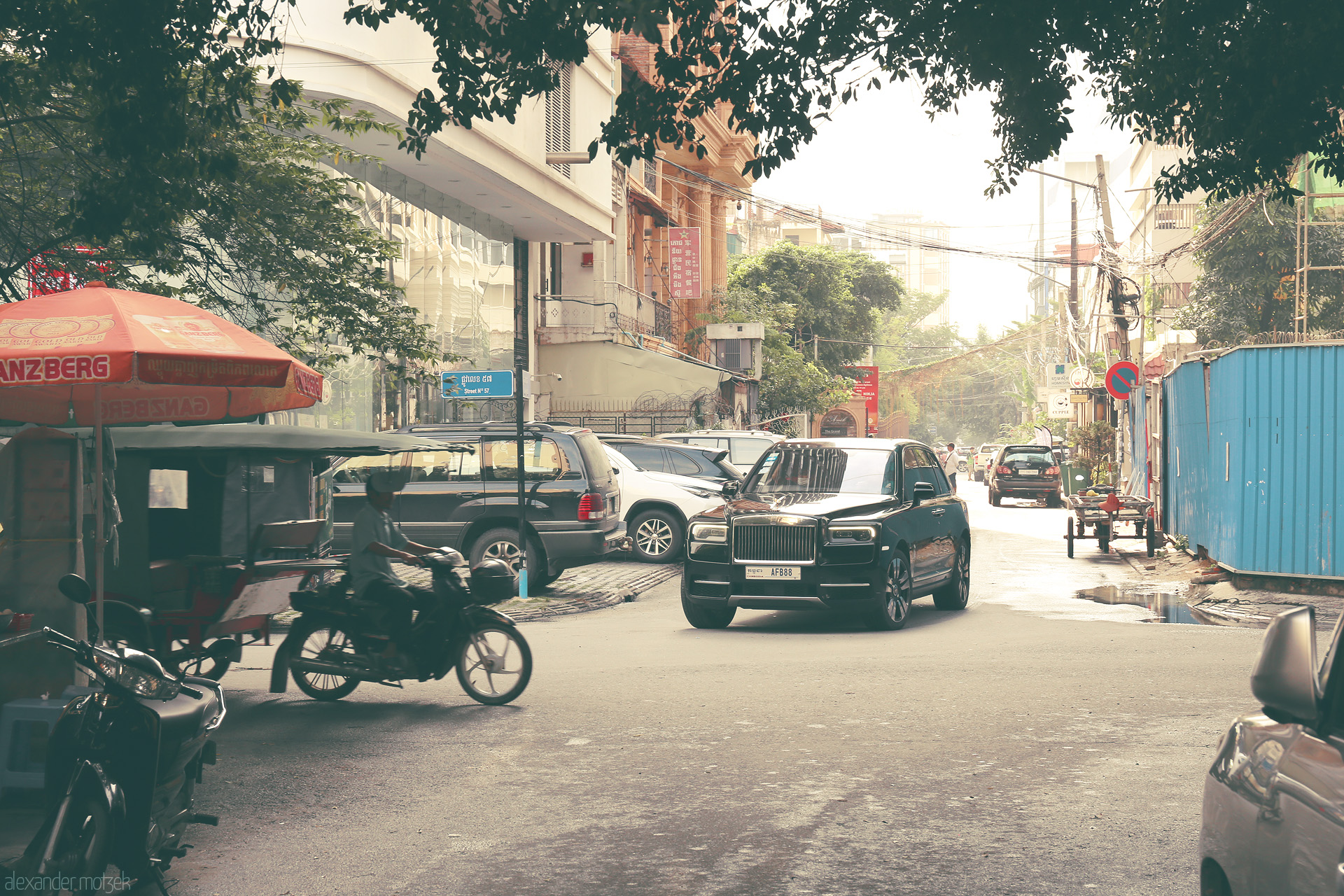 Foto von Luxury mingles with local life—Rolls-Royce, tuk-tuks, and street stalls, Phnom Penh’s bustling street scene under morning light.
