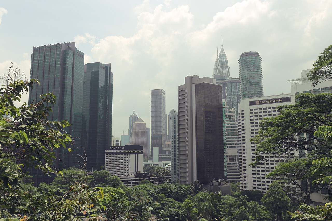 Petronas Whispers Foto von Explore the lush green meeting the soaring skyscrapers of Kuala Lumpur, crowned by the iconic Petronas Towers under a soft, cloudy sky.
