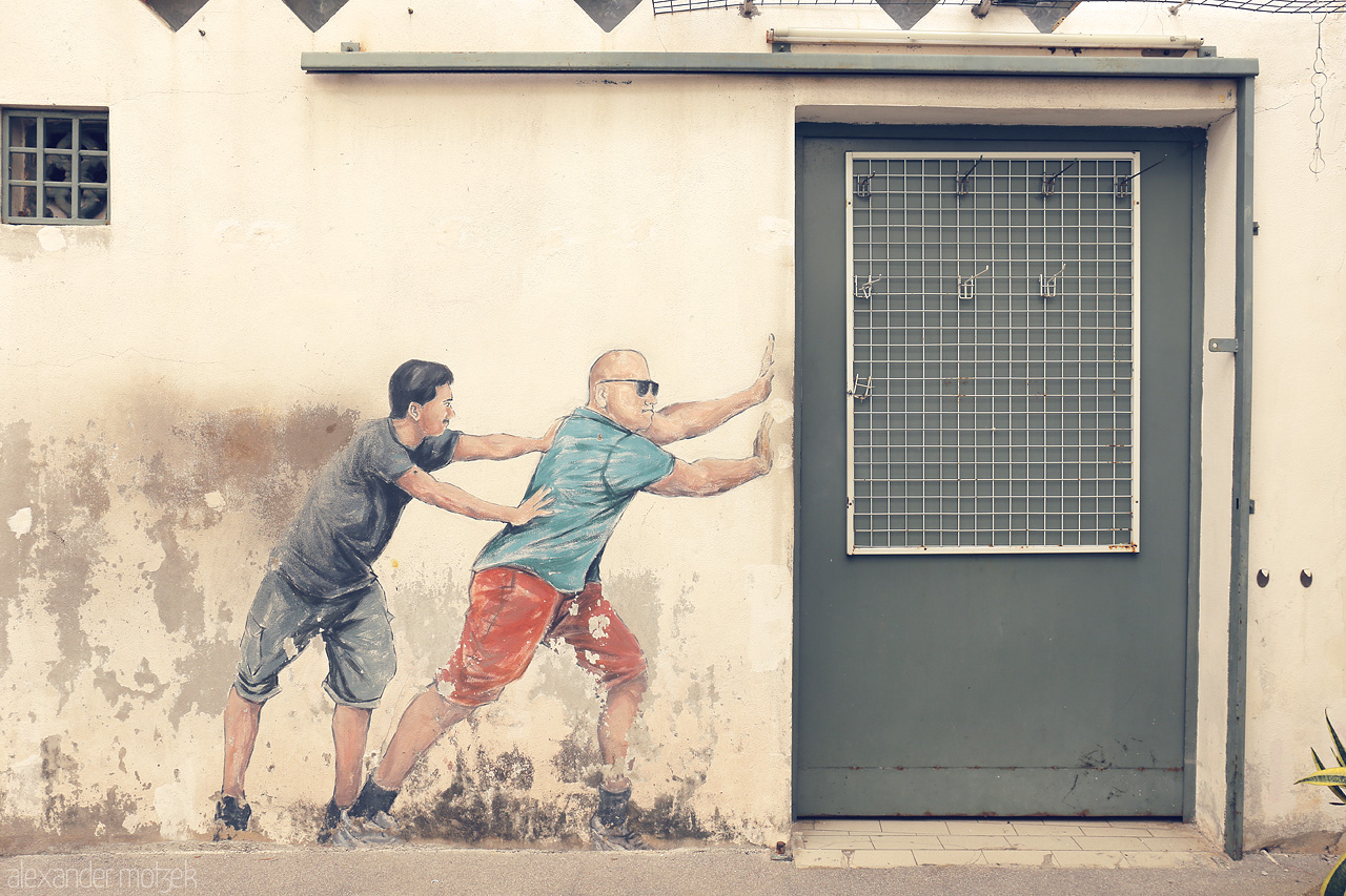 Street Canvas of Penang Foto von Street art in Penang, Malaysia, shows two figures pushing an actual door, blending reality with mural artistry in a whimsical urban scene.