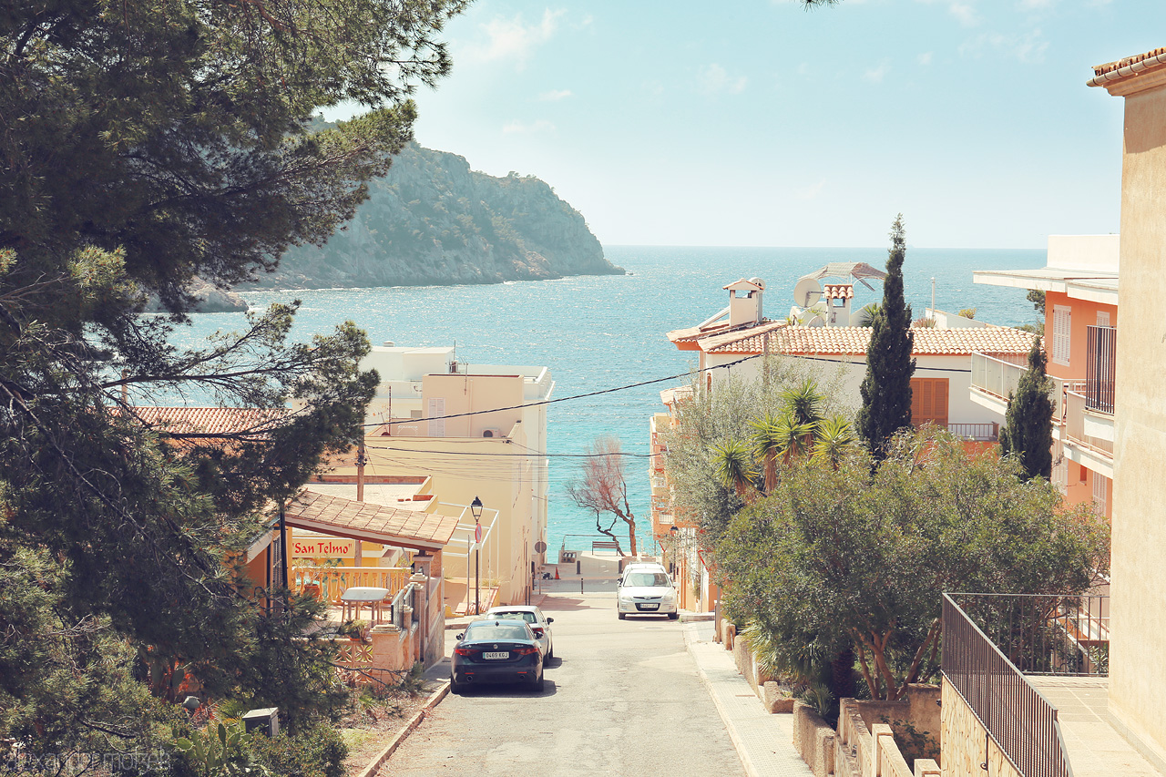 Balearic Breeze Foto von A serene glimpse down a tree-lined street in Sant Elm, Mallorca, leading to the azure Mediterranean Sea.
