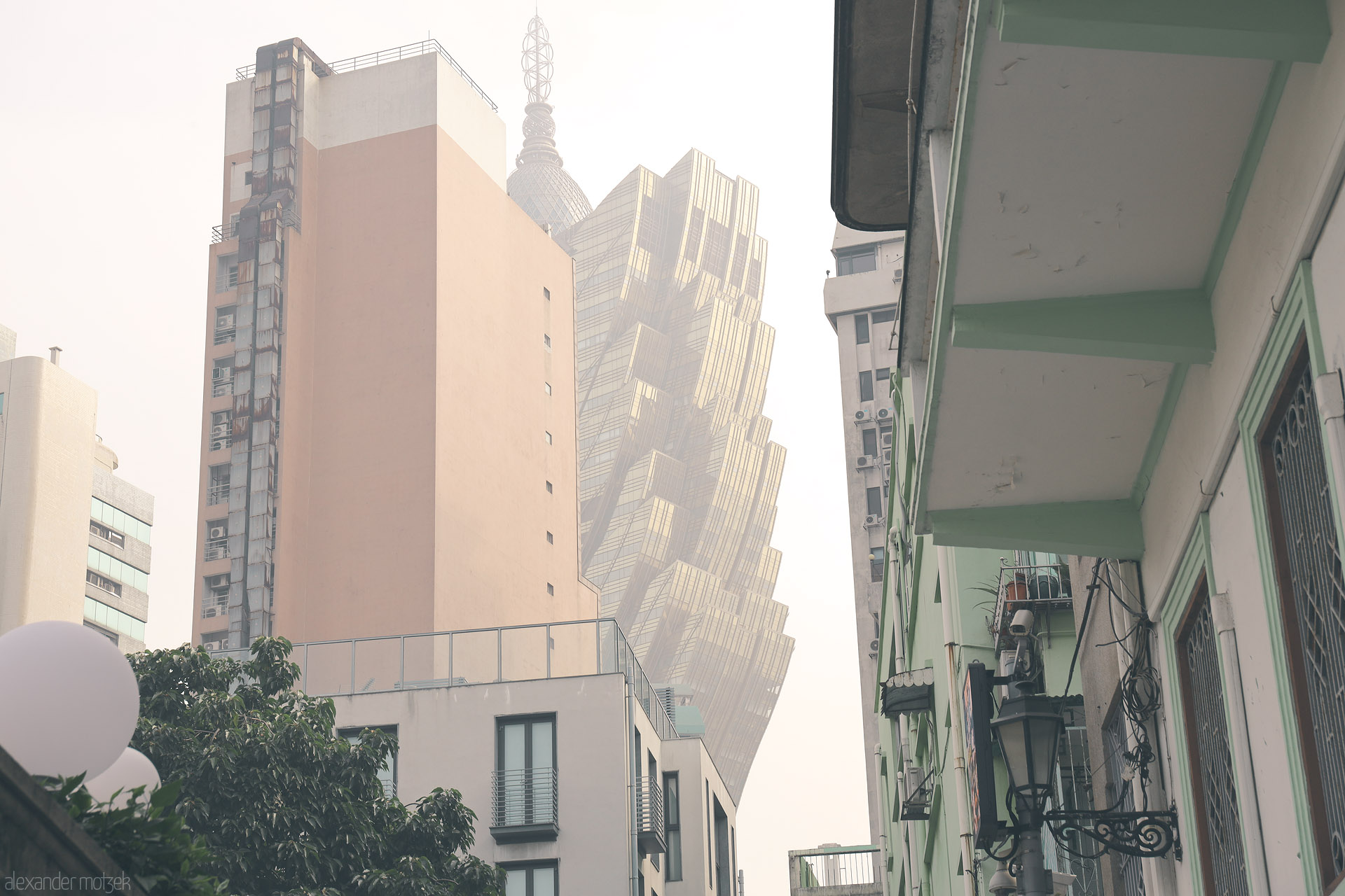 Foto von Pastel balconies frame the Grand Lisboa tower in soft haze—an old Macau lane meeting the futuristic skyline.