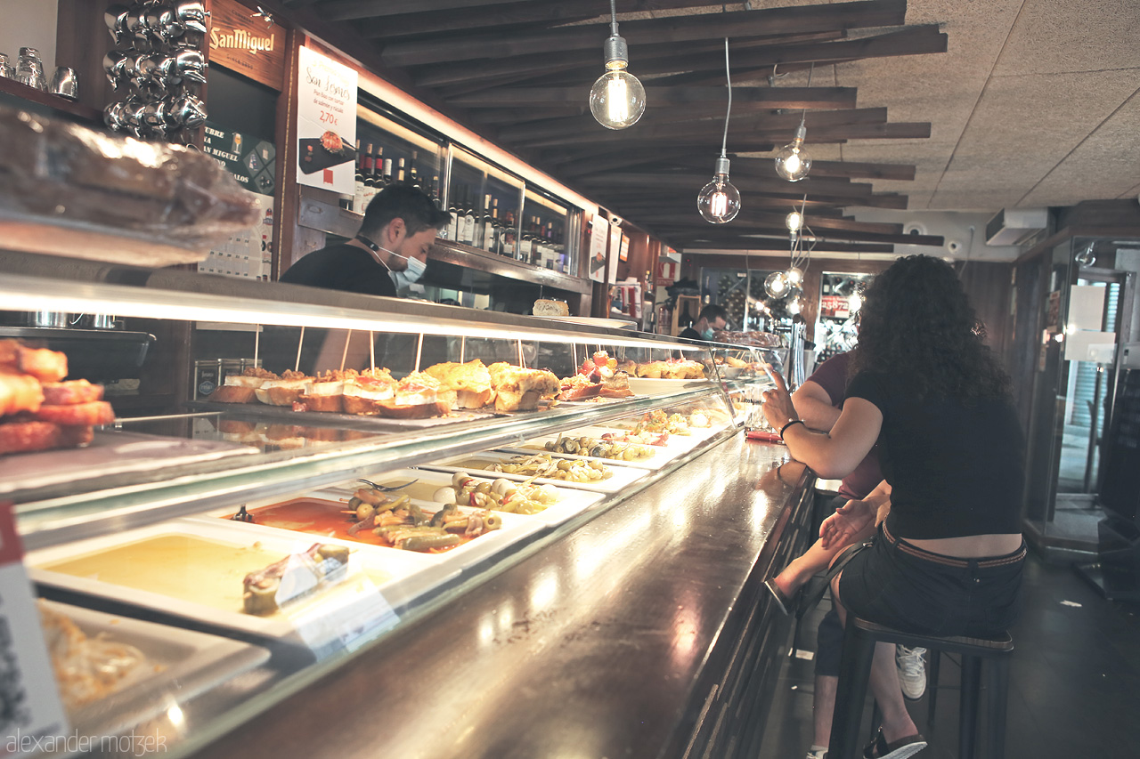 Pintxos de Burgos Foto von Patrons at a bar in Burgos, enjoying traditional Basque pintxos under warm ambient light.