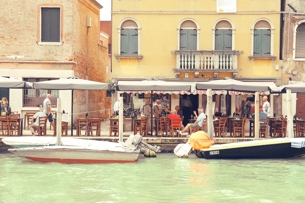 Gondola Gatherings Foto von Quaint café life unfolds by Venice's serene canals, boats bobbing as patrons savor the city's charm.