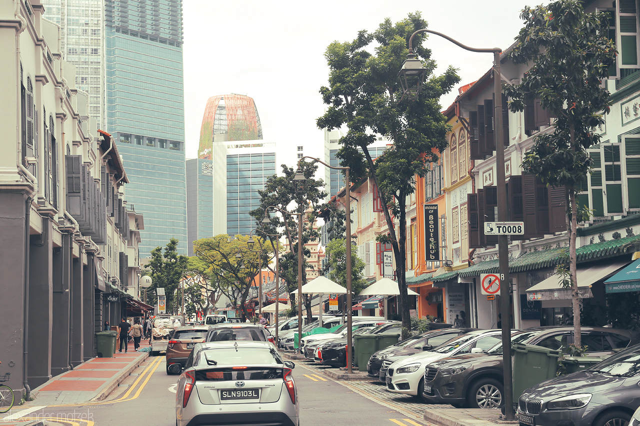 Kampong Kleinod Foto von A charming street in Singapore's Kampong Glam, where heritage shophouses meet modern skyscrapers under a tropical urban canopy.