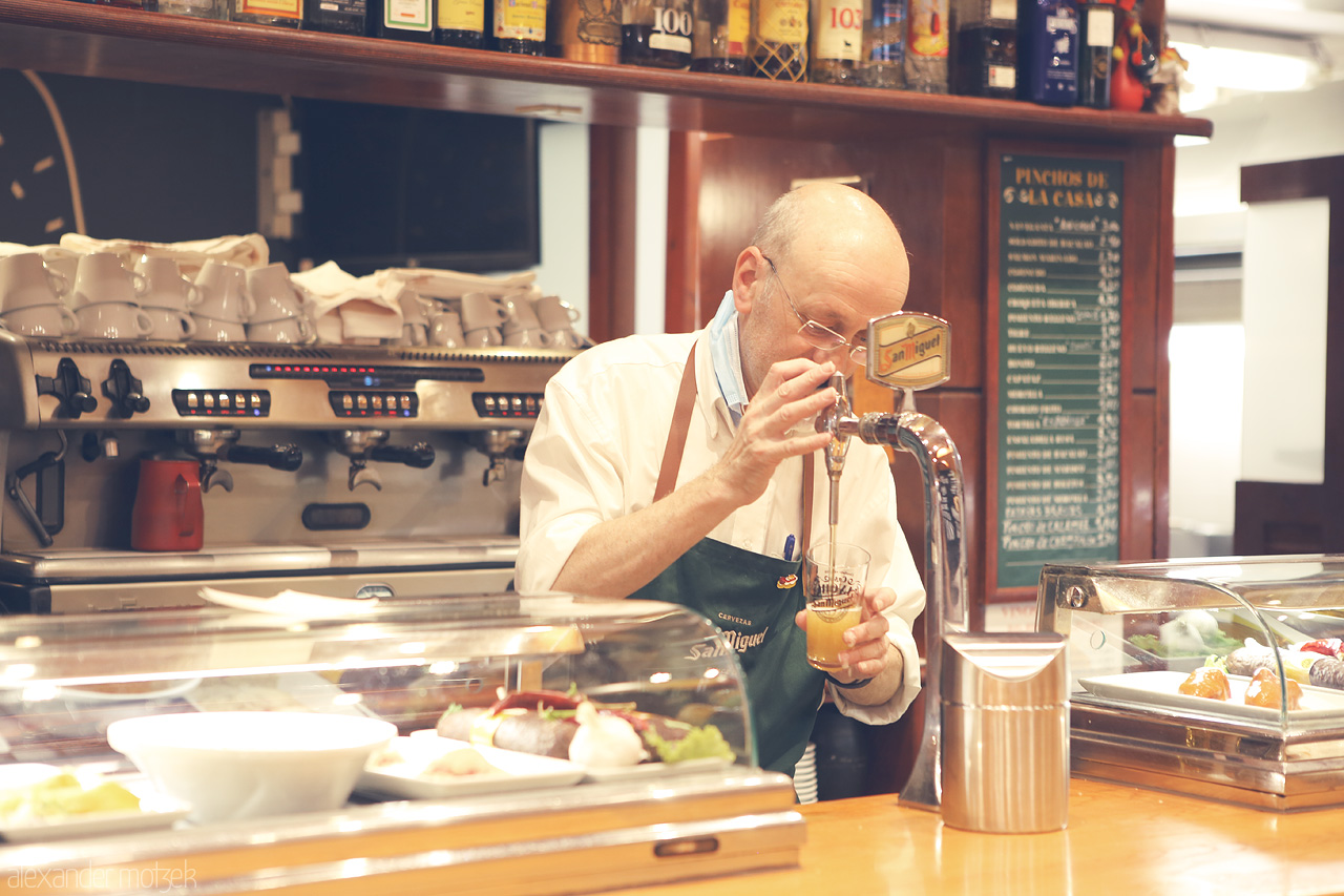 Foto von A bartender in Burgos, Spain, pours and examines a beer amidst a quaint pinchos bar setting.