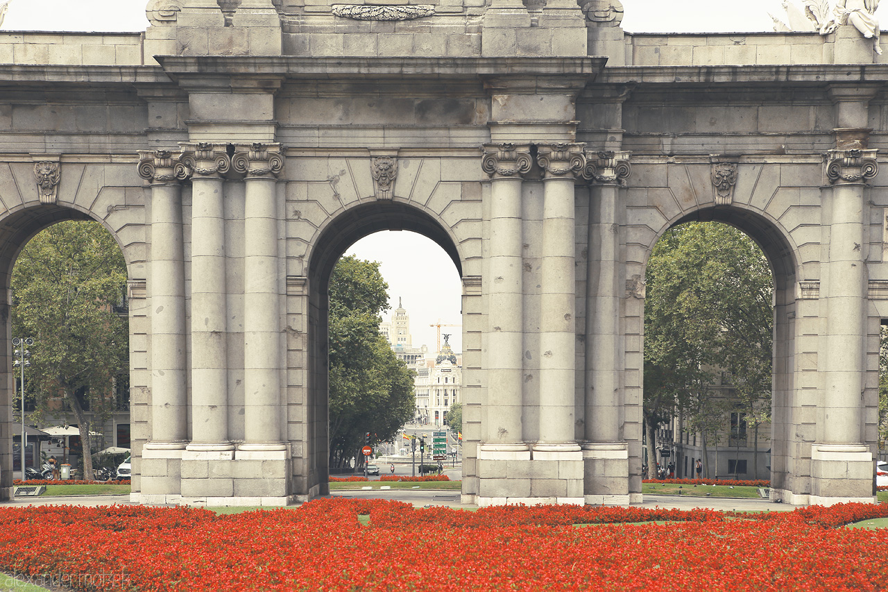 Arcos de Madrid Foto von Stone archways frame city life amidst vibrant red flowers, a serene snapshot of Madrid's grandeur.