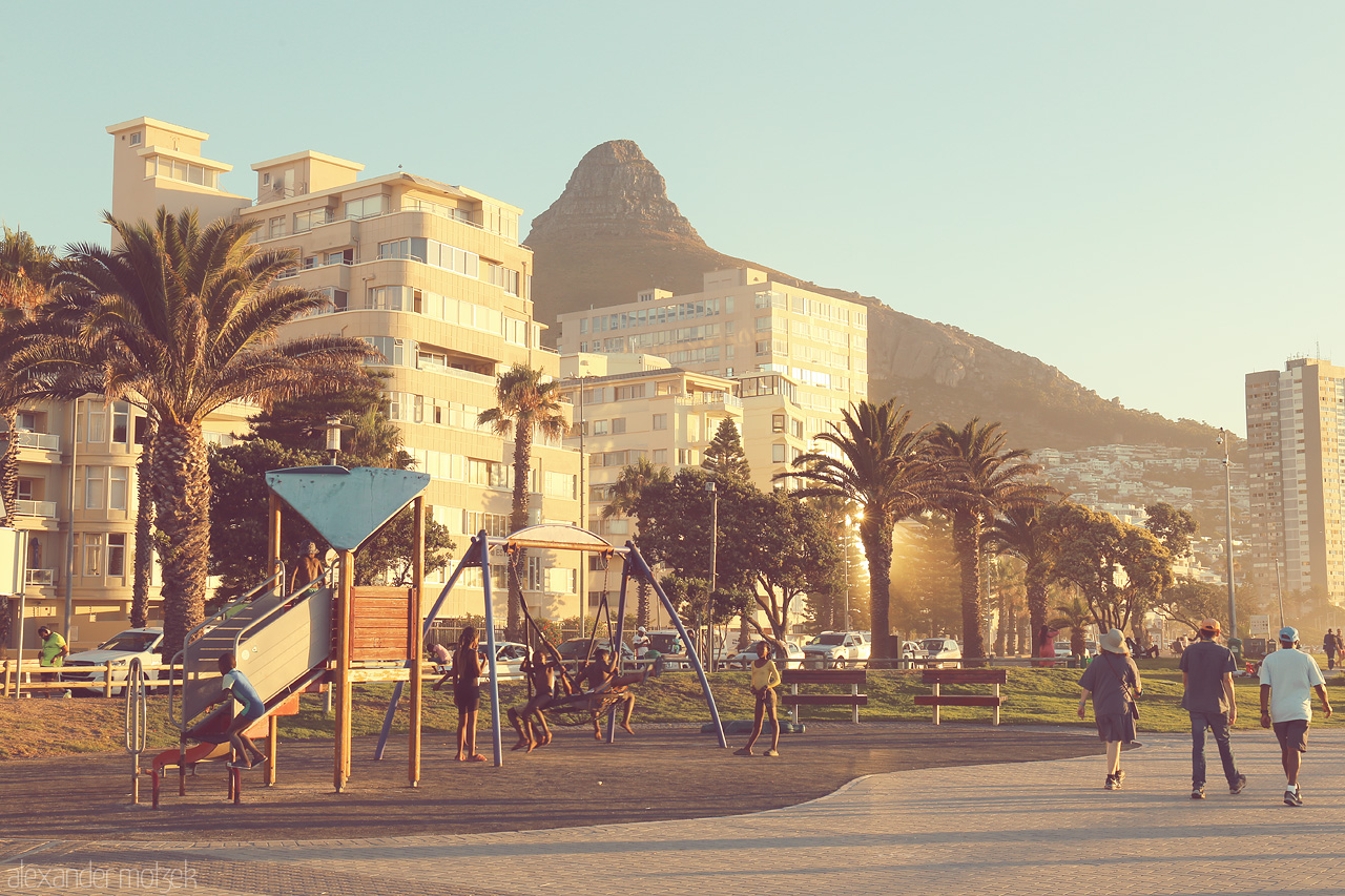 Seaside Stroll at Sunset Foto von Sunset glow on Cape Town's coastline with Lion's Head watching over and playful swings bringing joy to the promenade.