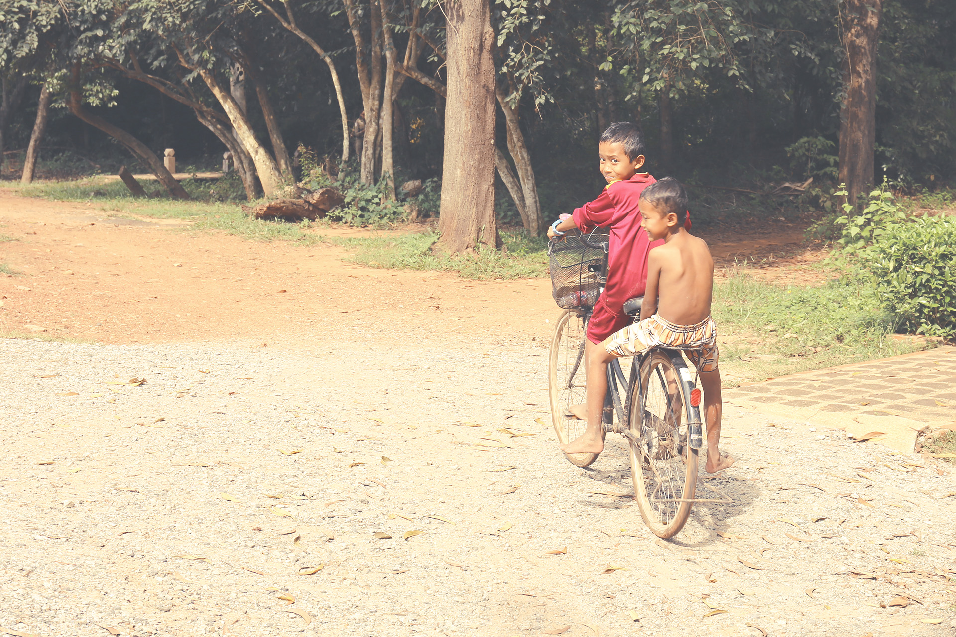 Foto von Two young boys share a bike, laughter, and a sunlit path near Angkor Wat, Siem Reap—where Khmer innocence and adventure meet.