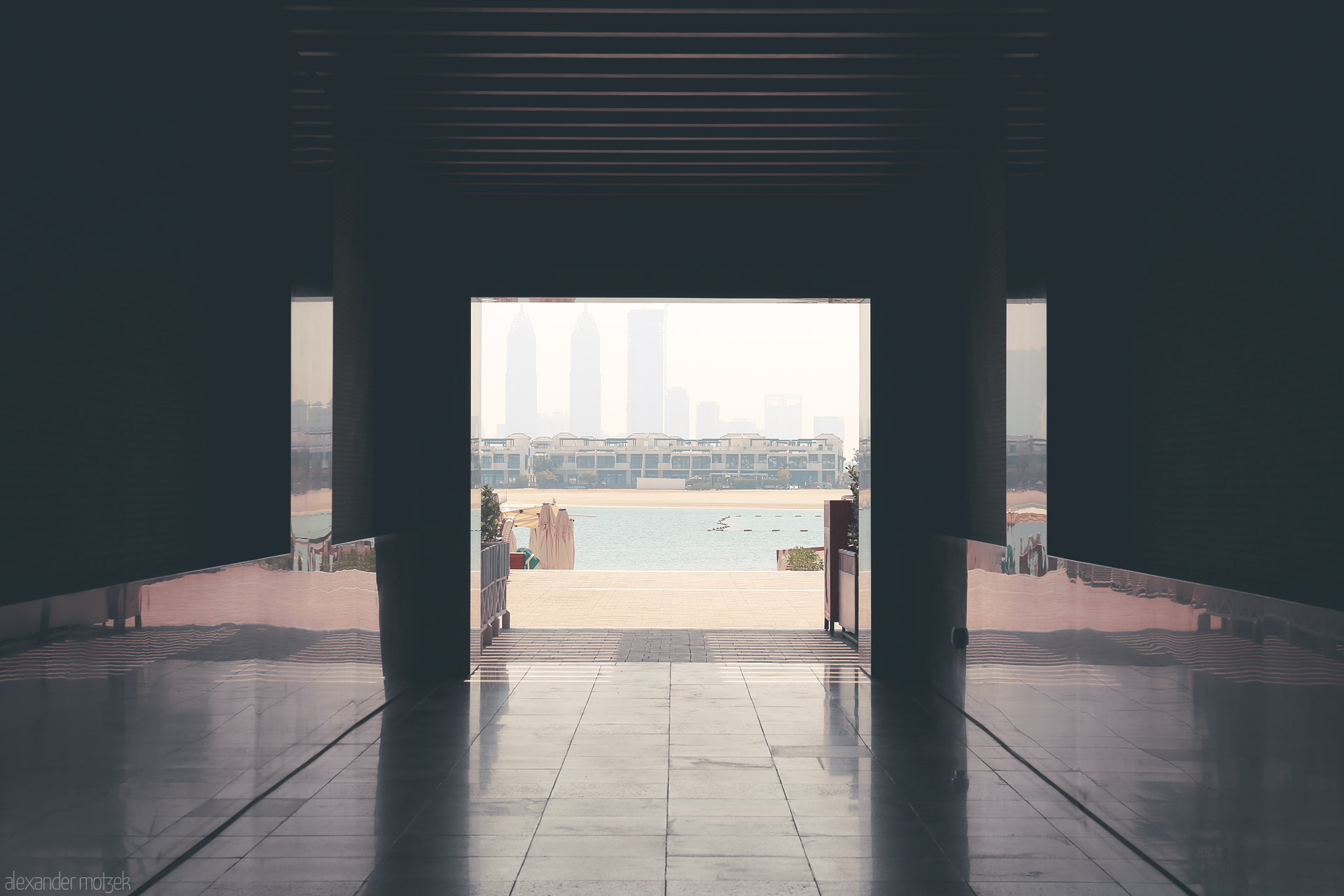 Foto von Through shaded hallways, Dubai’s skyline shimmers beyond Palm Jumeirah’s waterfront—a tranquil view wrapped in sunlit haze.