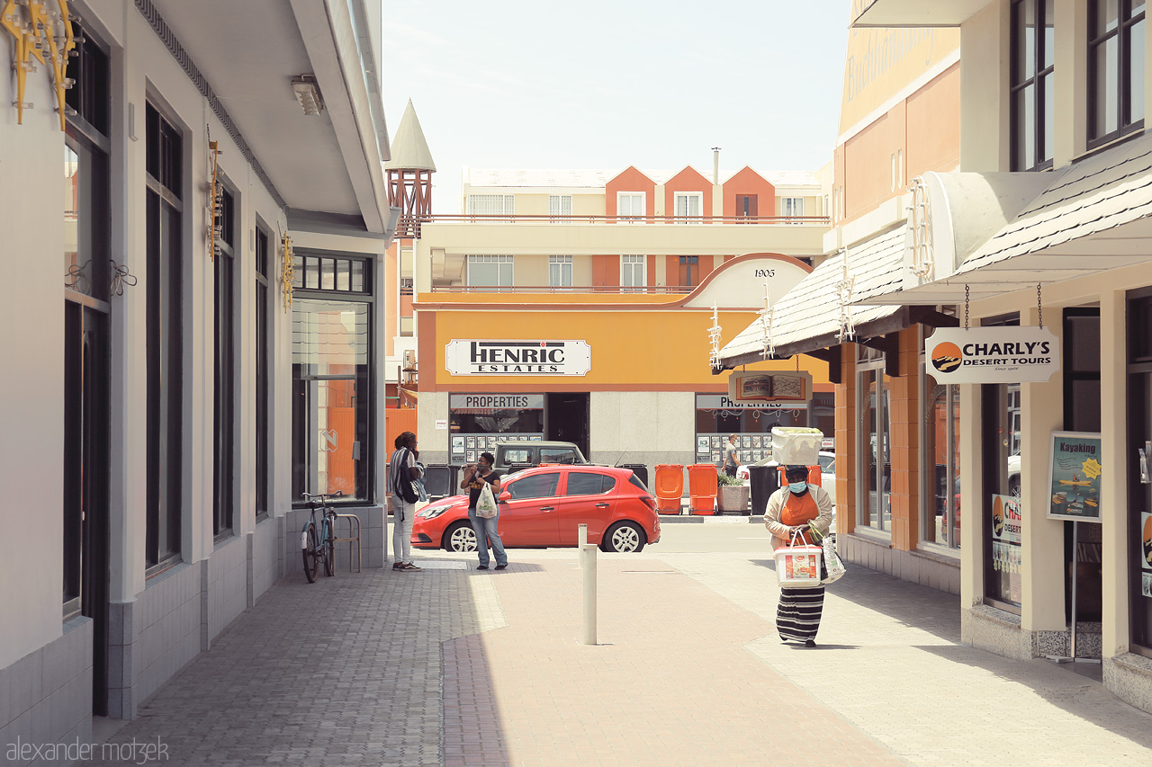 Swakopmund Sights Foto von Urban street in Swakopmund under a clear blue sky, showing architecture, a bright red car, and local passerby.