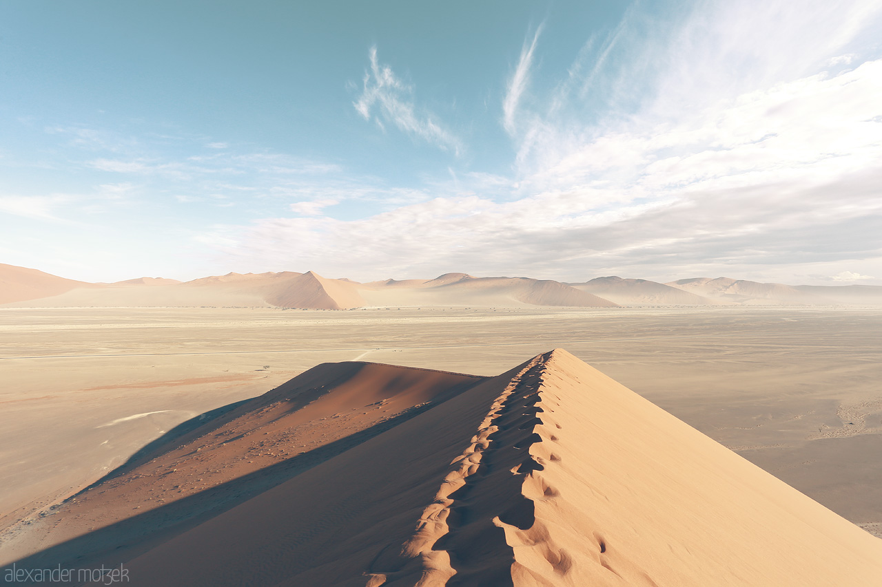 Namib's Crest Foto von Vastness of Sossusvlei - textured dunes juxtapose serene skies in Namibia's desert scape.