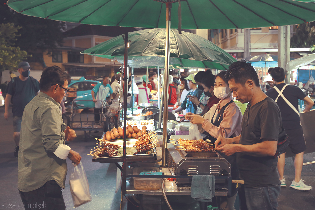 Talat Twilight Tastes Foto von Vibrant street food scene at Talat Yot, Bangkok. Locals delight in skewers and snacks under the glow of green umbrellas.