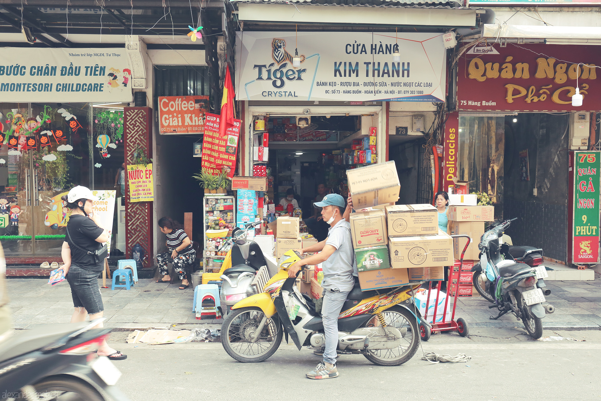 Boxes & Bánh Keo Foto von A deliveryman balances boxes on a motorbike, weaving through the vibrant bustle of Hàng Buom, Hanoi’s iconic street life.