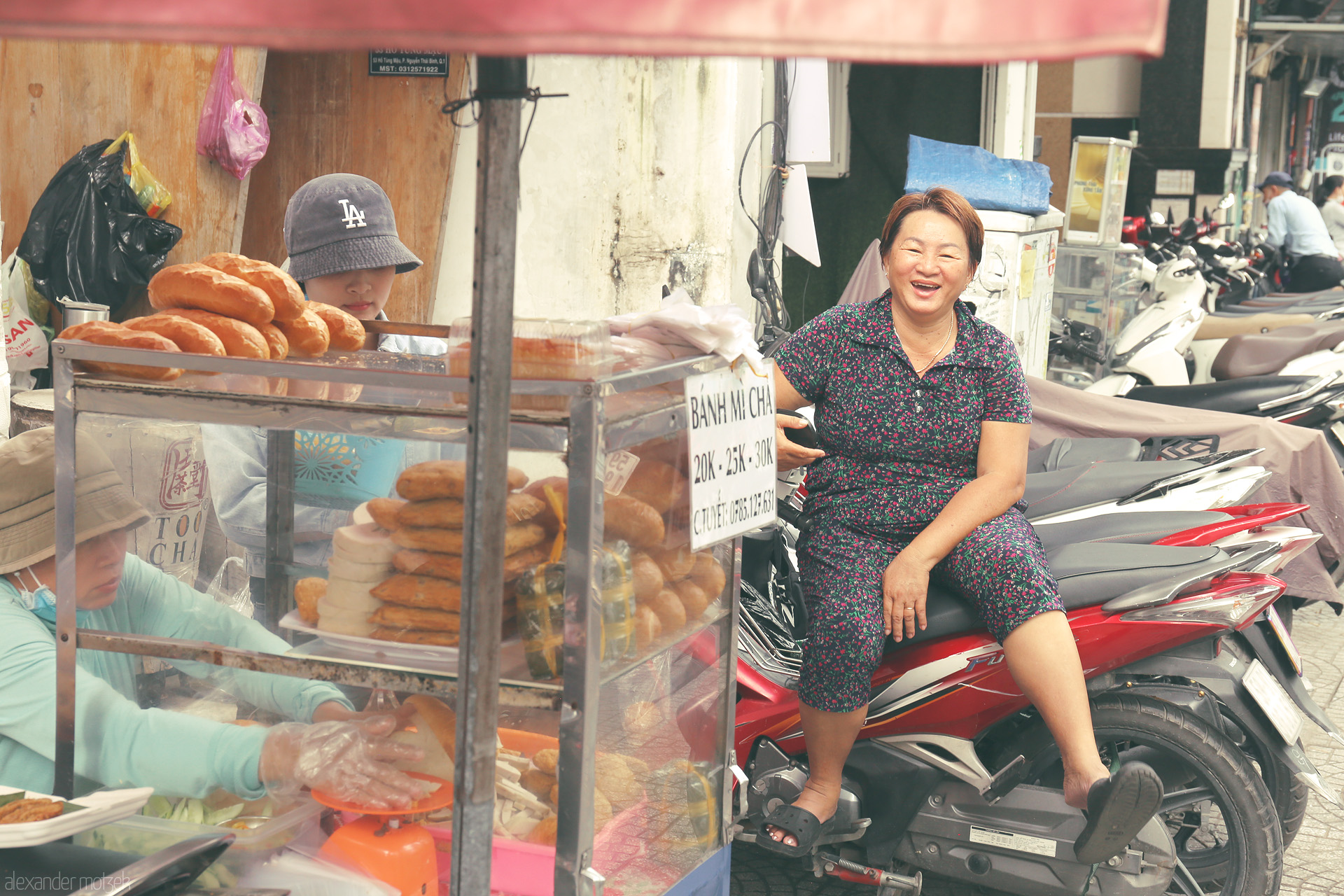 Saigon Bánh Mì Bliss Foto von A joyful vendor relaxes beside a bánh mì cart in bustling Ho Chi Minh City, Vietnam, street life alive with flavor and laughter.