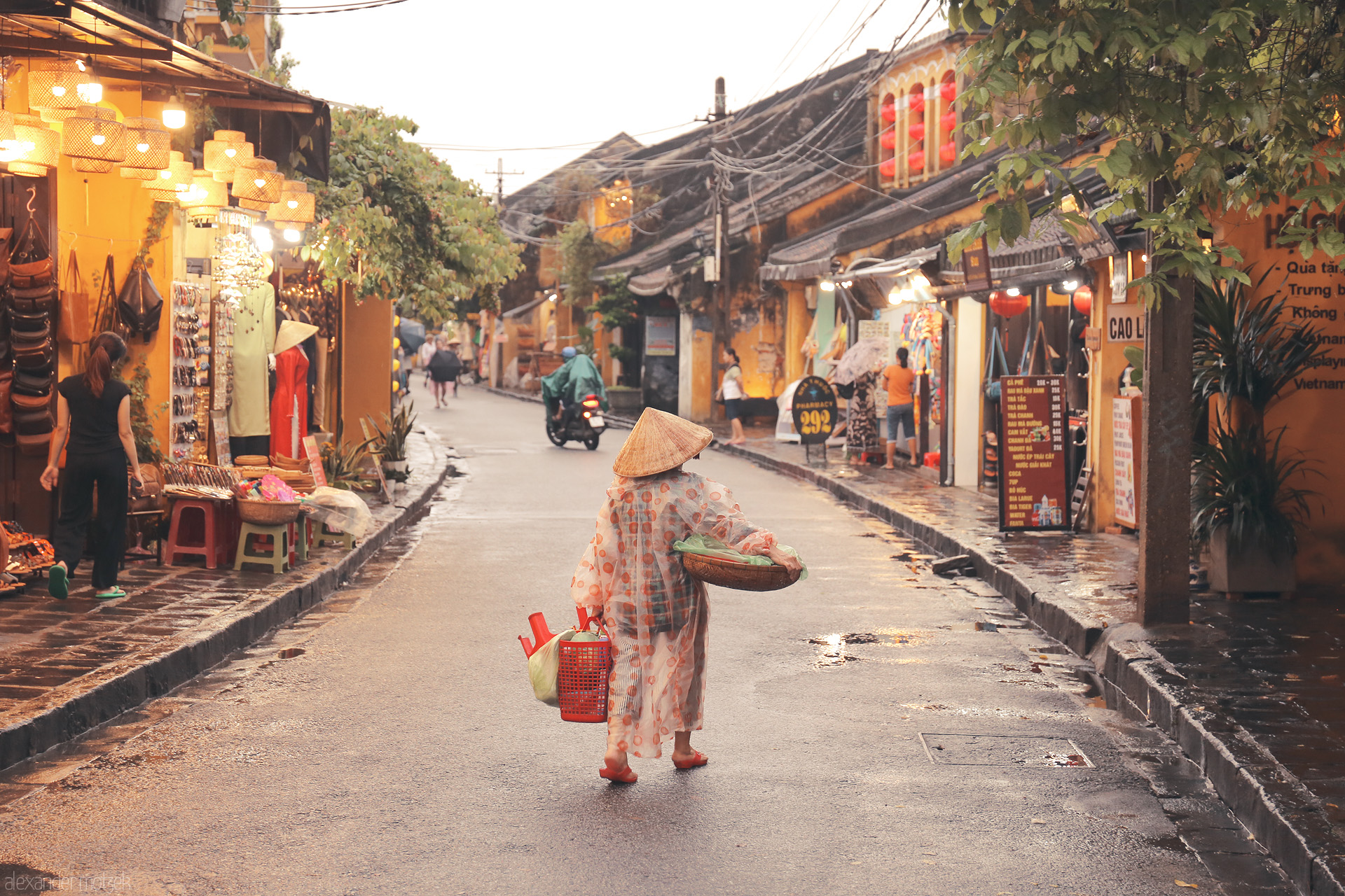Lantern Lane Reverie Foto von A lone vendor, bathed in golden light, strolls rainy Hoi An streets under lanterns and conical hats; daily life in Vietnam’s ancient town.