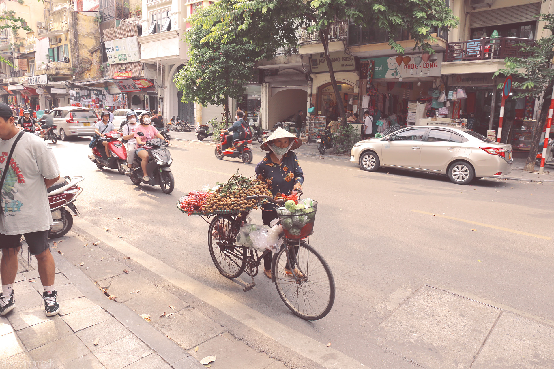The Longan Seller Foto von A street vendor with a fruit-laden bicycle navigates the vibrant Old Quarter in Phuong Hàng Gai, Hanoi.