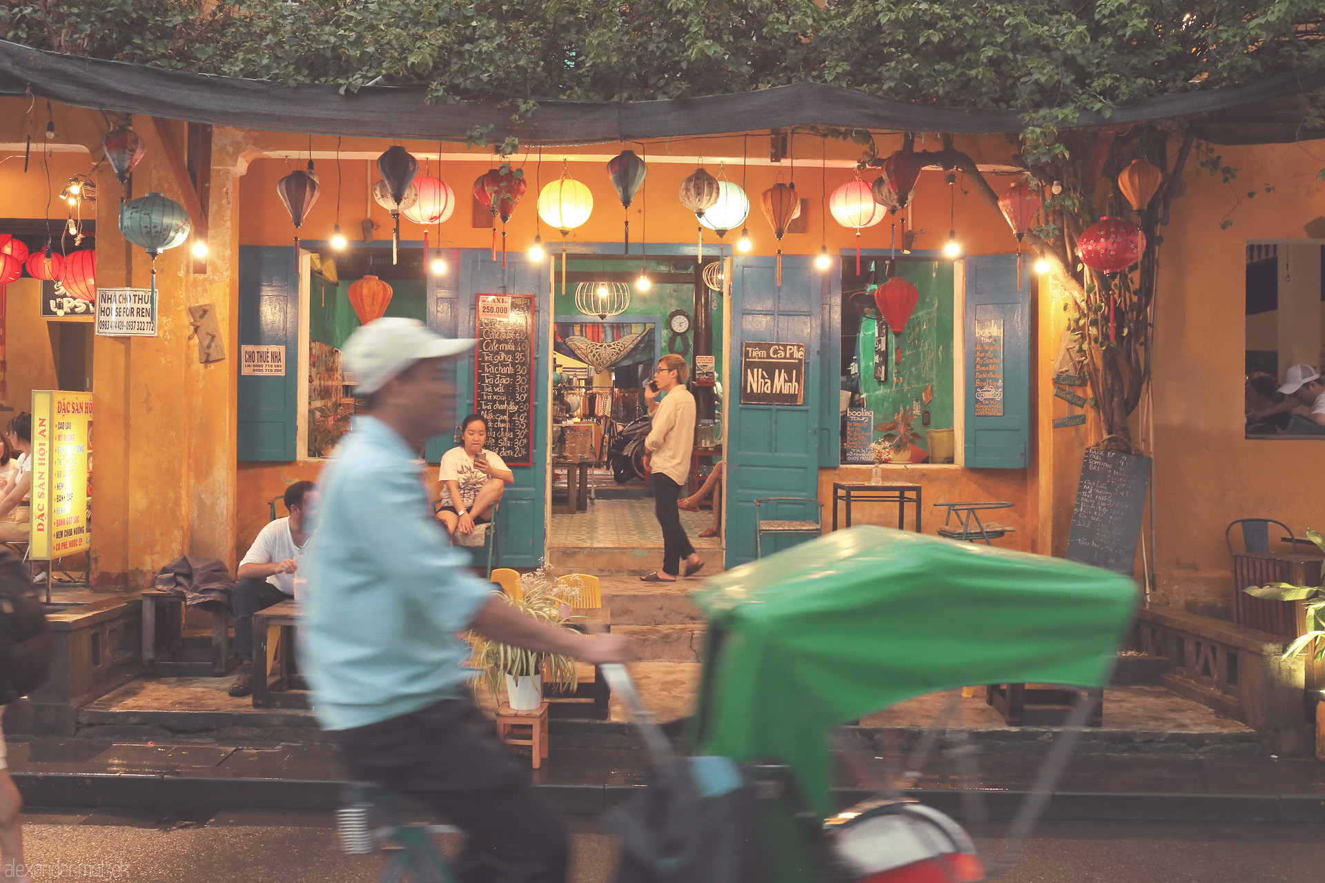 Lantern Lull in Hoi An Foto von A vibrant Hoi An café glows beneath colorful lanterns as a cyclo glides past, capturing the city's charm and evening bustle in Vietnam.